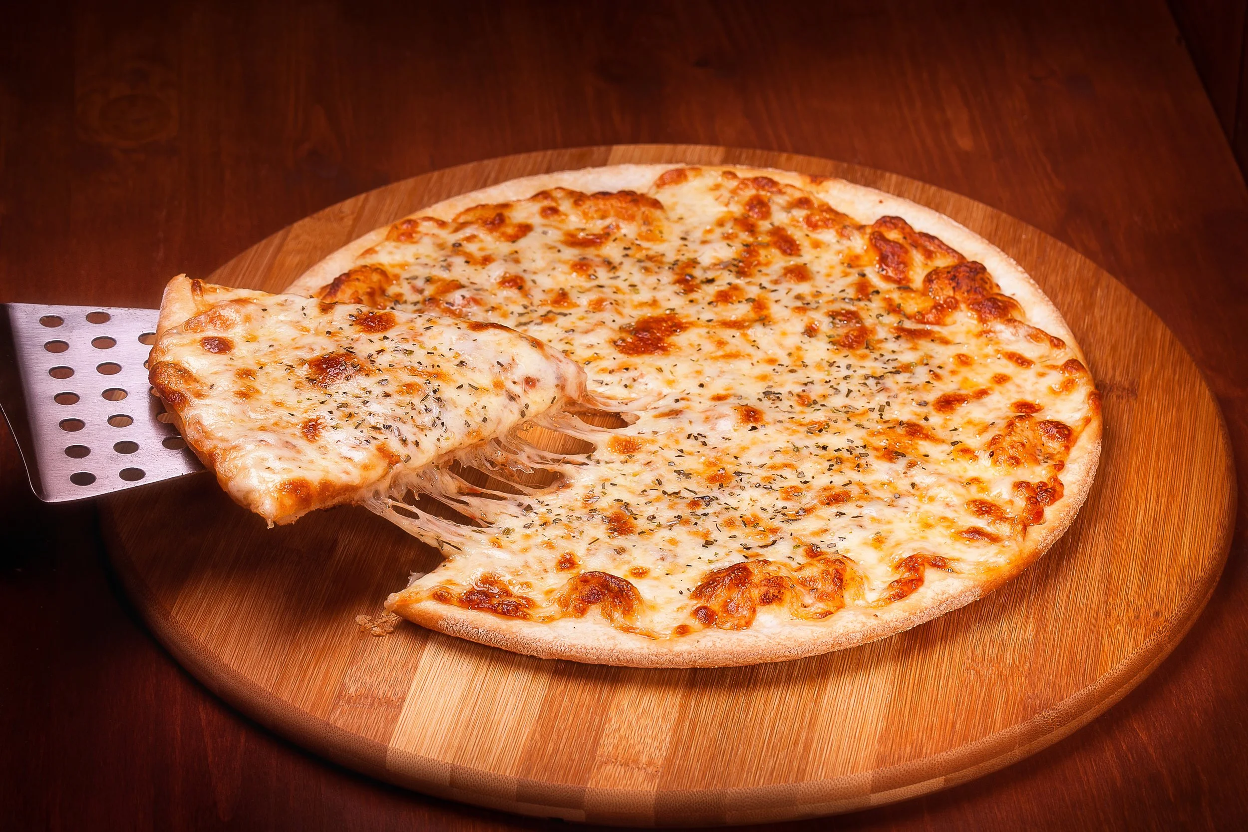 Cheese pizza on a wooden serving board with a slice being lifted, melted cheese and herbs visible.