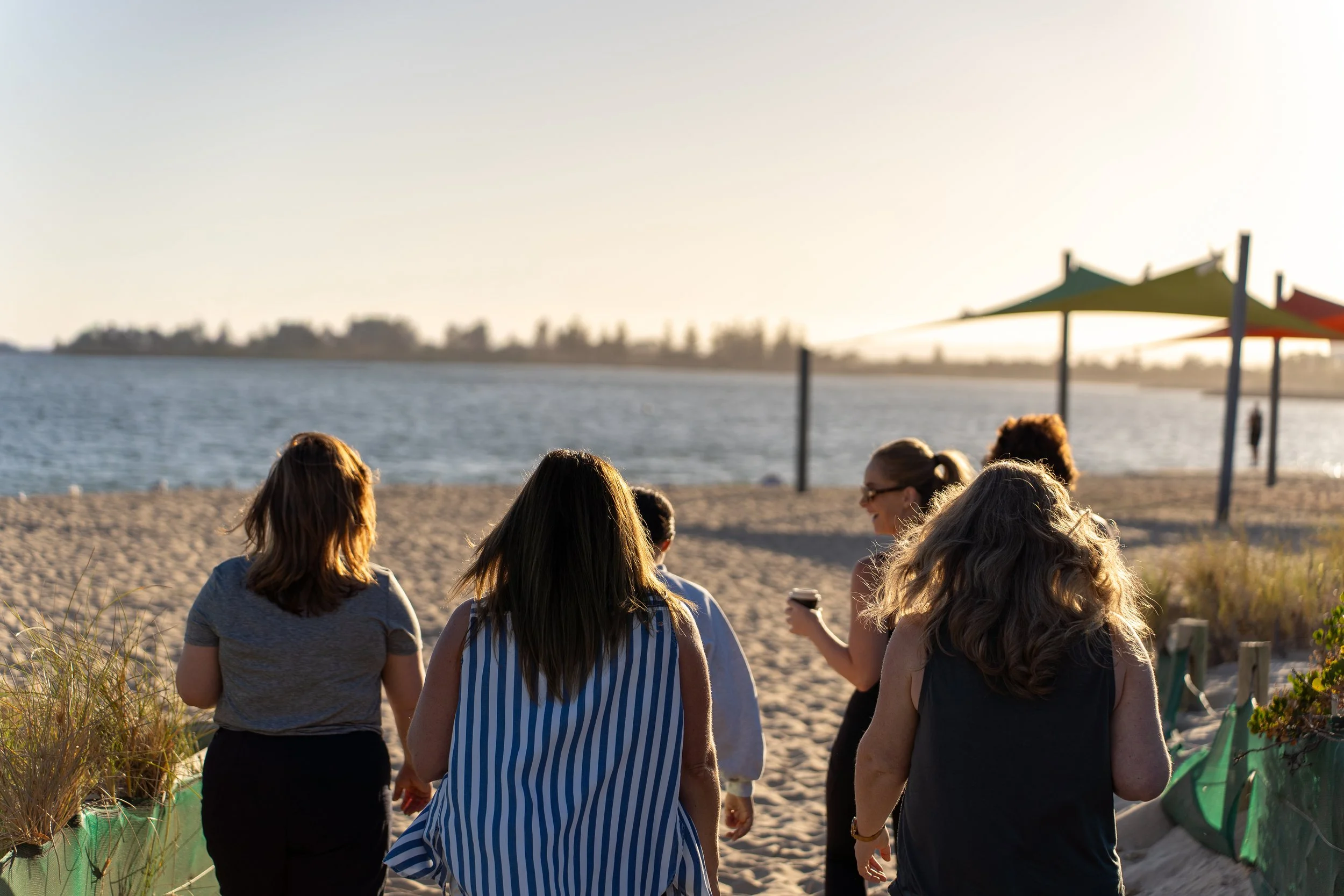Group of women walking on the beach near water, with umbrellas in the background