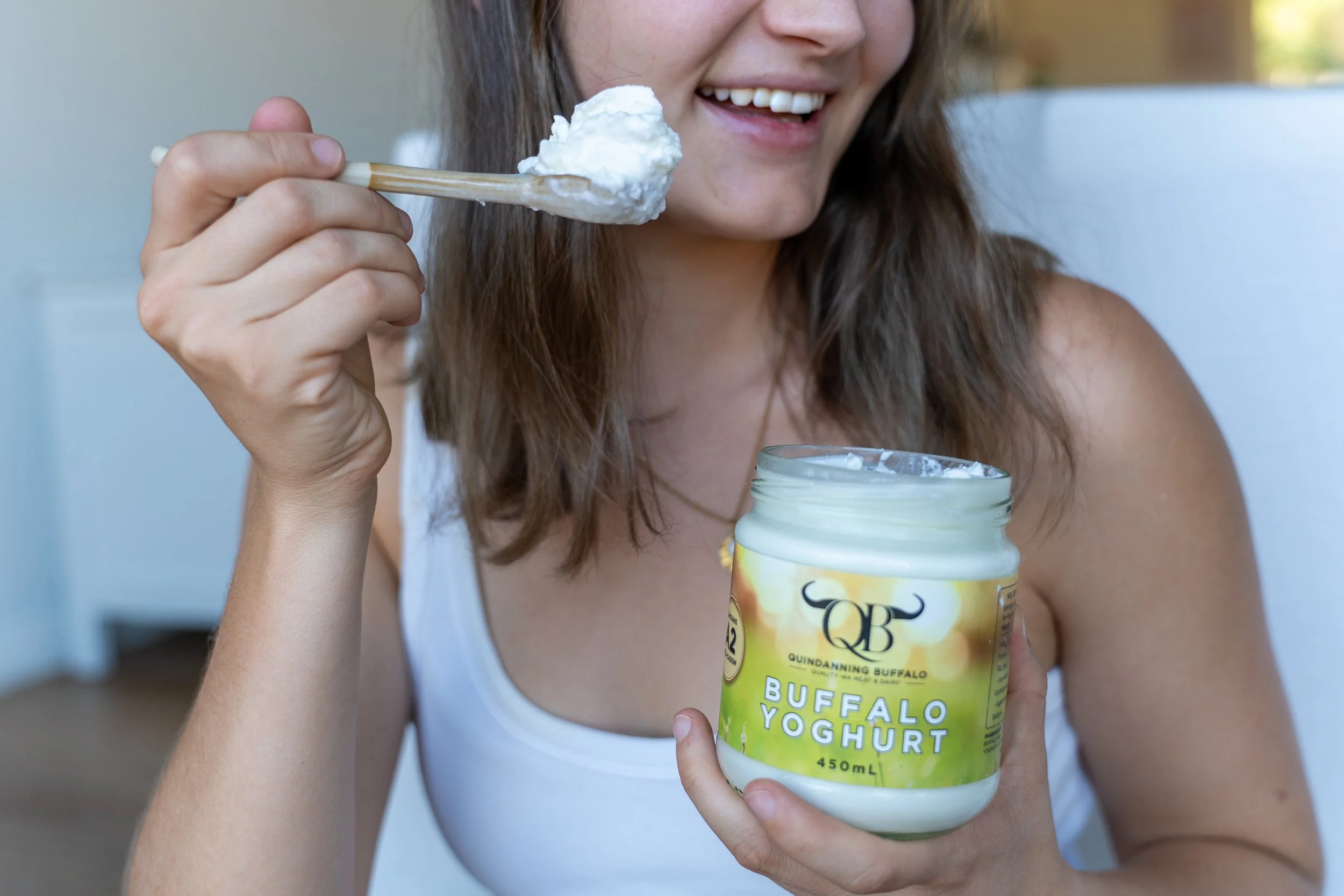 Woman holding jar of Buffalo Yoghurt with one hand and eating it with a spoon in the other hand.