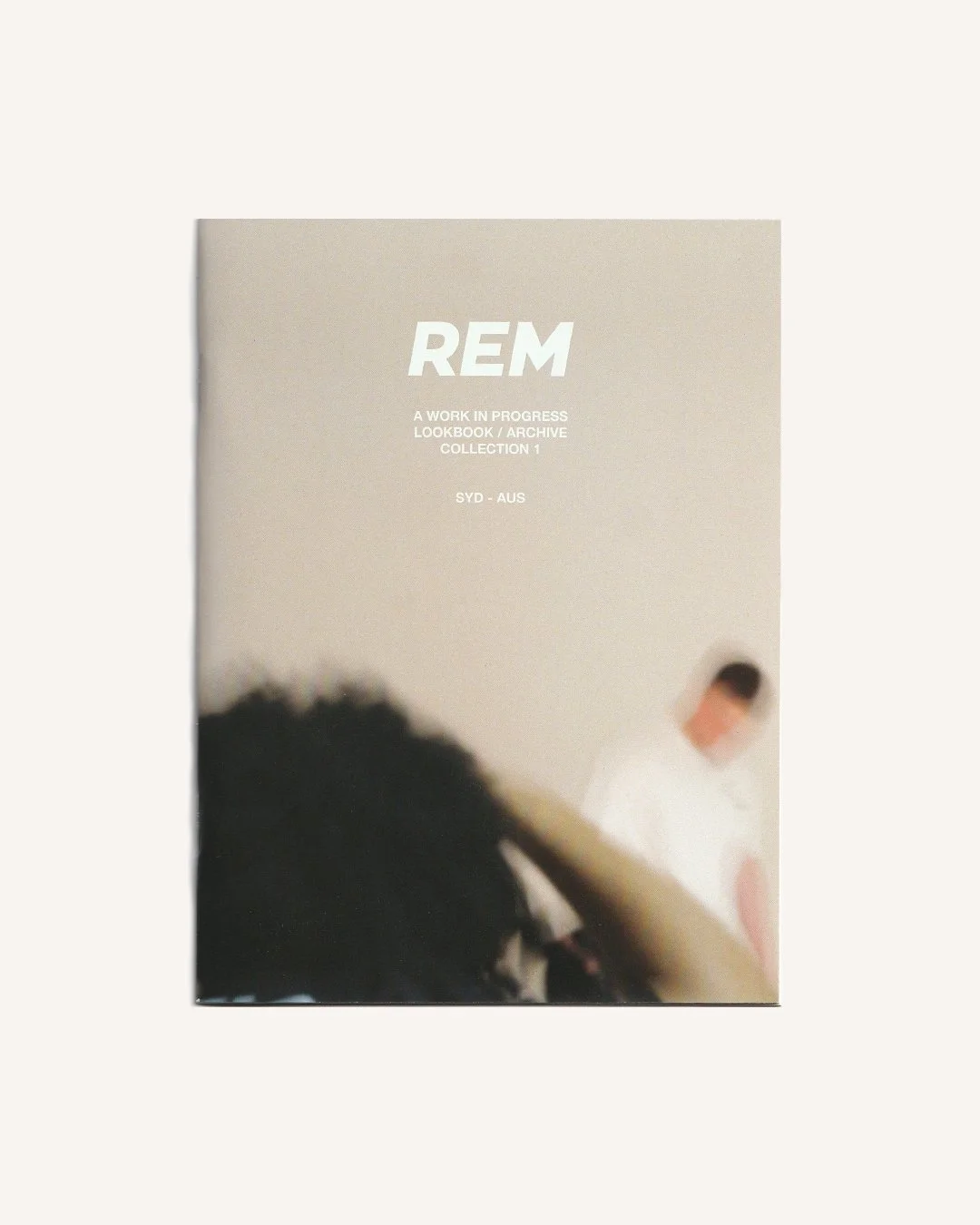 Cover of a book or magazine titled 'REM' with subtitle 'A Work in Progress Lookbook / Archive Collection 1' and locations SYD - AUS, featuring a blurred image of a person and some curly hair in the background.