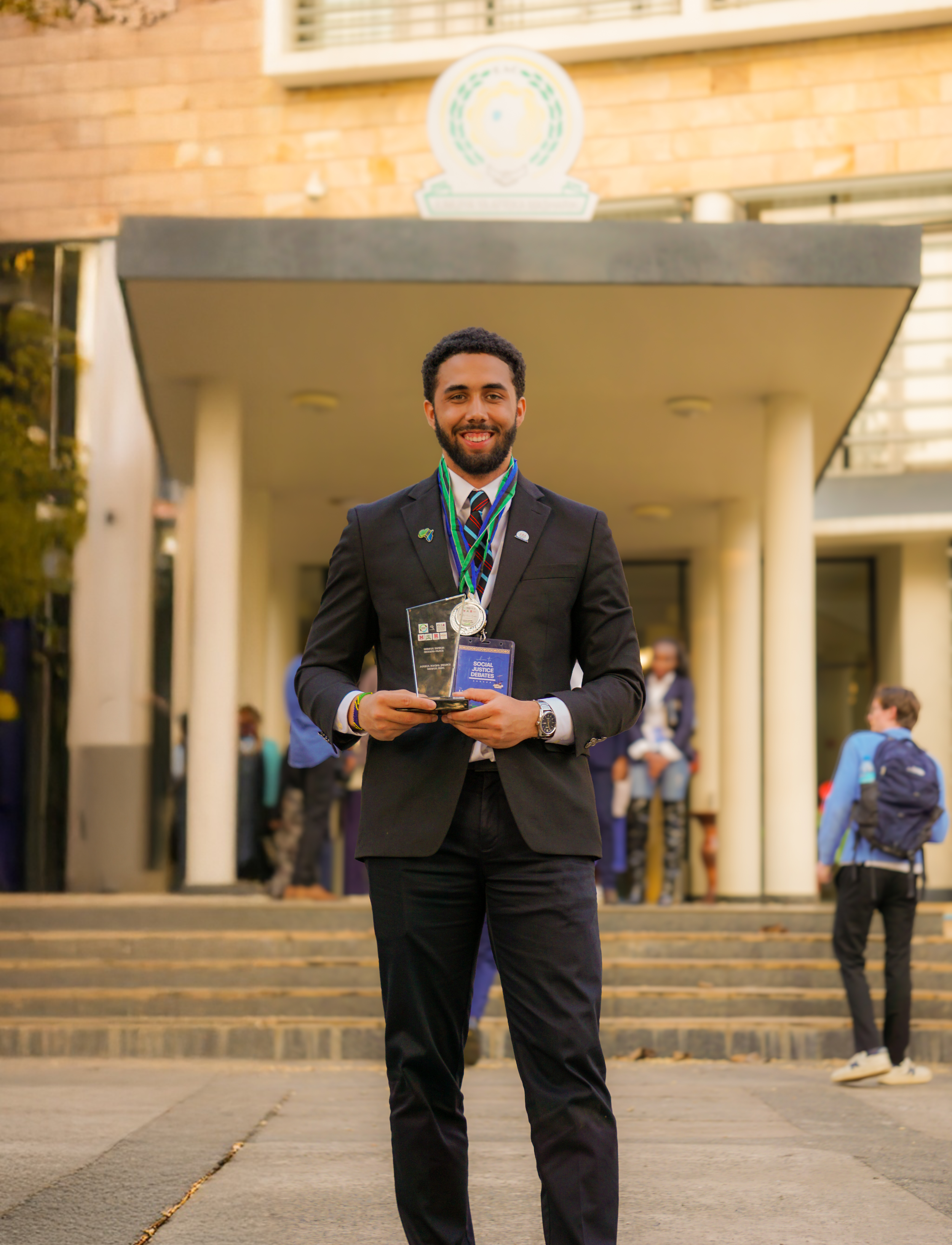 Javen Sears celebrating second place and Second Best Speaker at the East African Community (EAC) headquarters in Arusha, Tanzania, holding his trophies representing the University of Vermont Lawrence Debate Union.