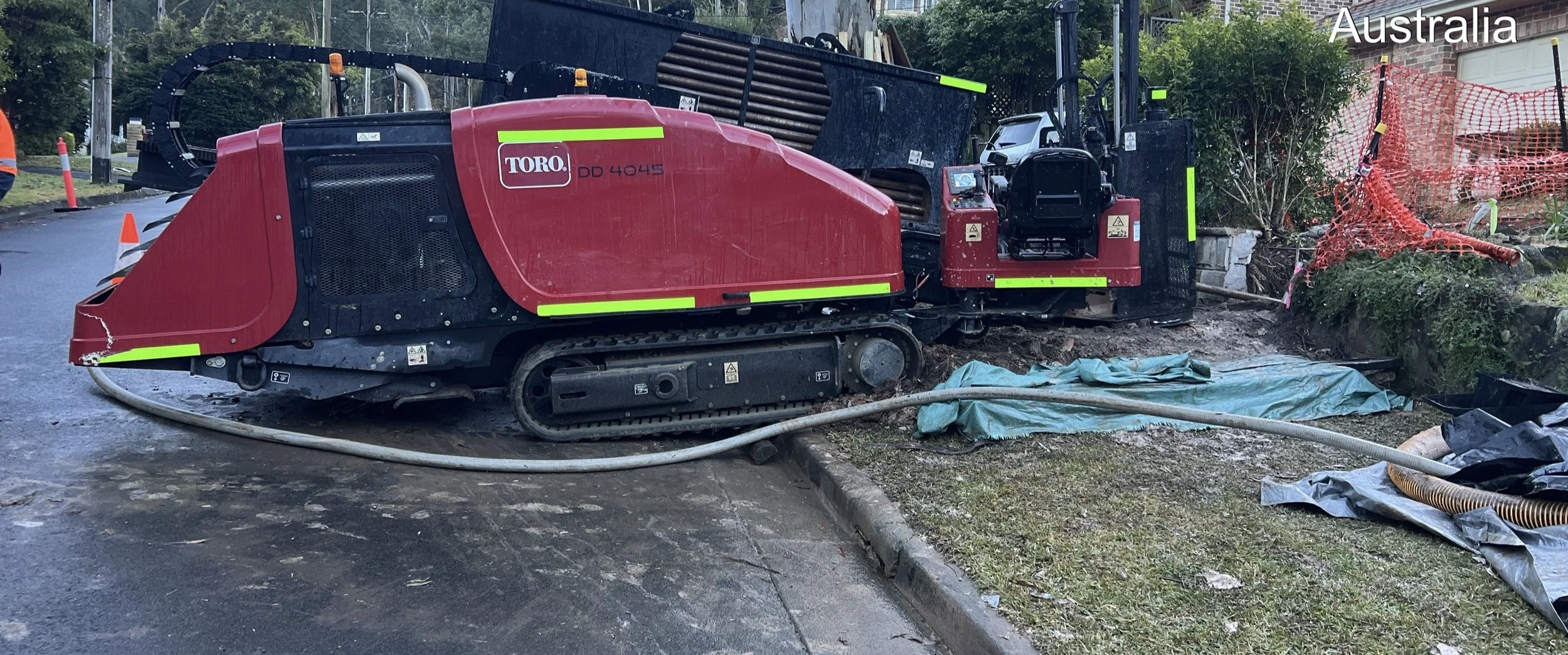 Construction site in Australia with a red Toro DD 4045 asphalt milling machine on a partially paved road surrounded by construction equipment, safety barriers, and protective materials.