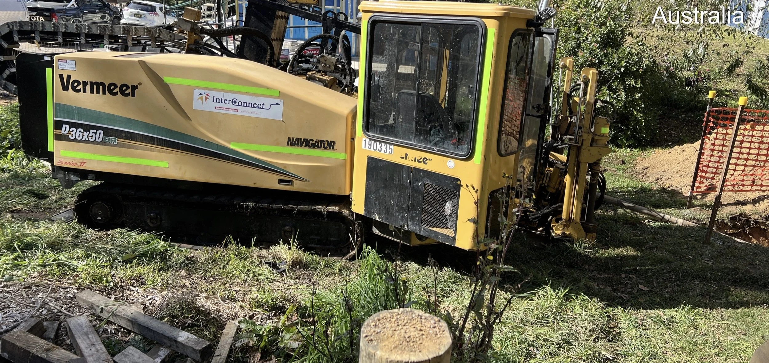 A small yellow and black Vermeer Navigator D36x50 DR trenching machine on a grassy area, with trees and a construction fence in the background, marked with Australian text and labels.