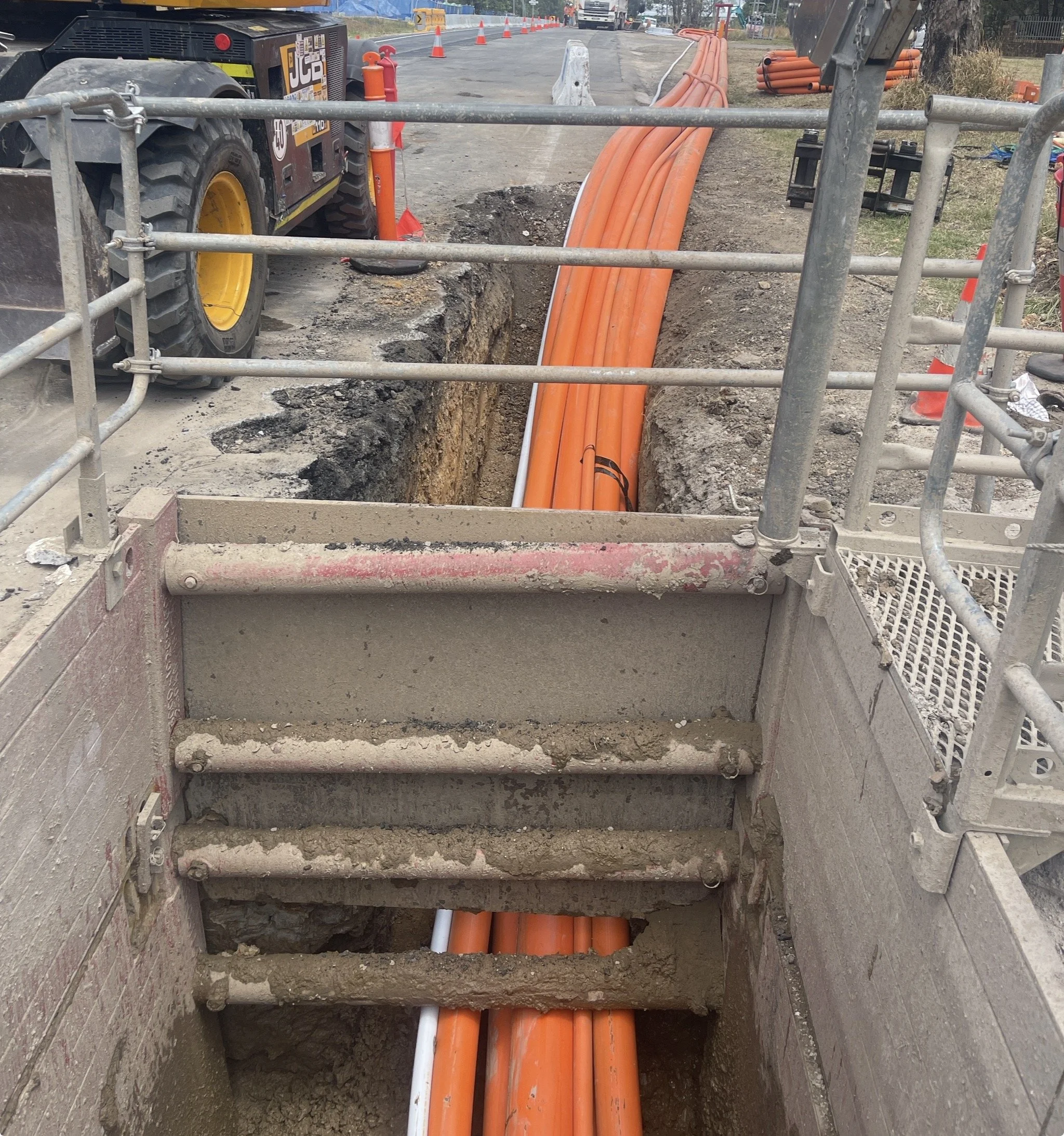 Construction site with orange pipes laid underground, surrounded by dirt and heavy machinery.