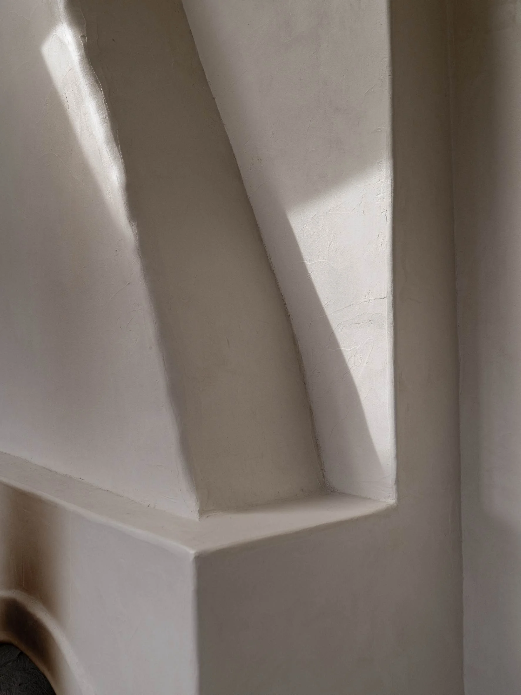 Close-up of a whitewashed wall with a decorative arch and a shadow cast across it.