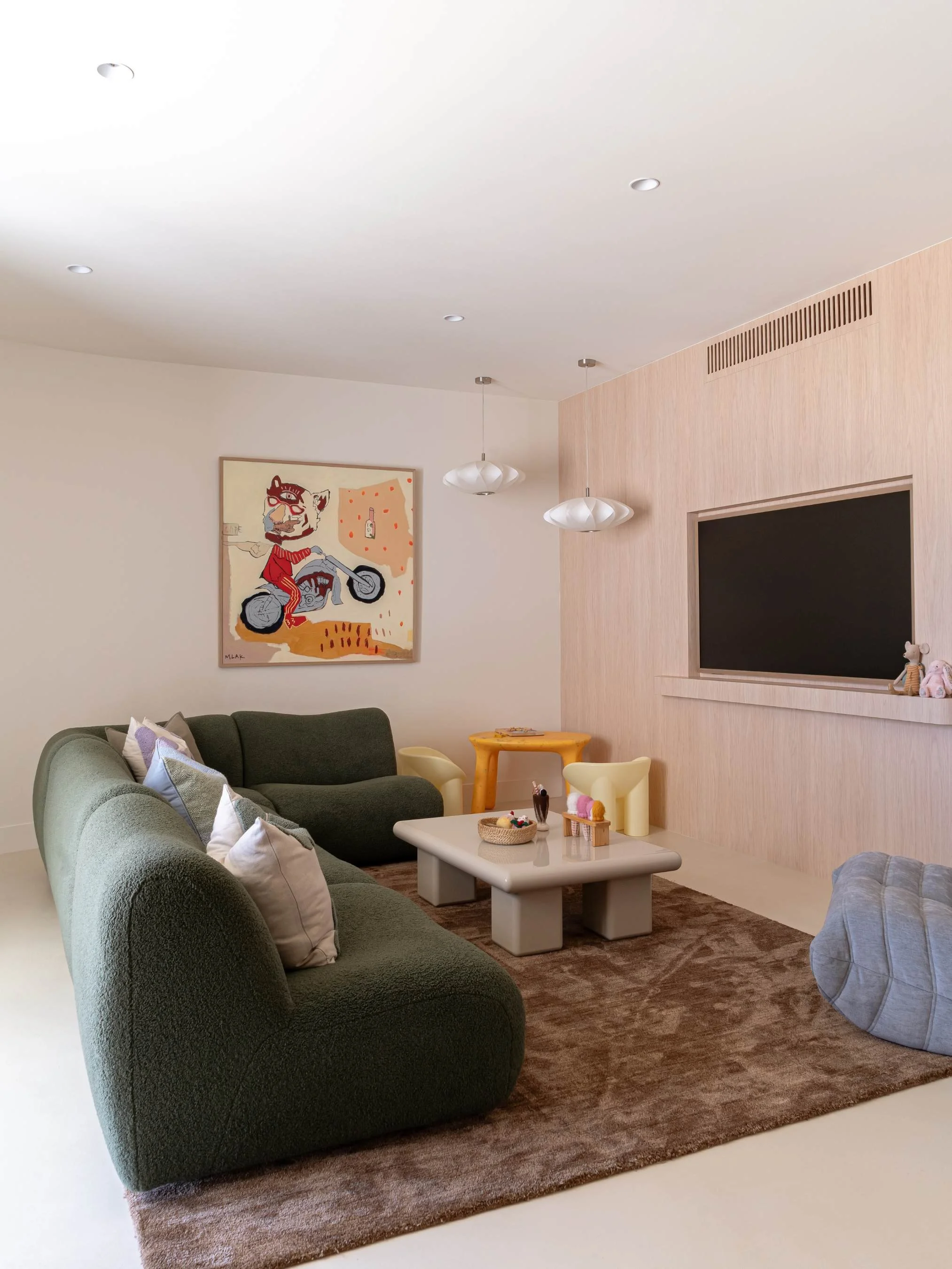 Modern living room with green and dark green sofas, decorative pillows, a beige coffee table, playful yellow and cream chairs, a brown rug, a wall-mounted TV, and abstract wall art in the Ocean Ave Project in Tweed Heads, QLD