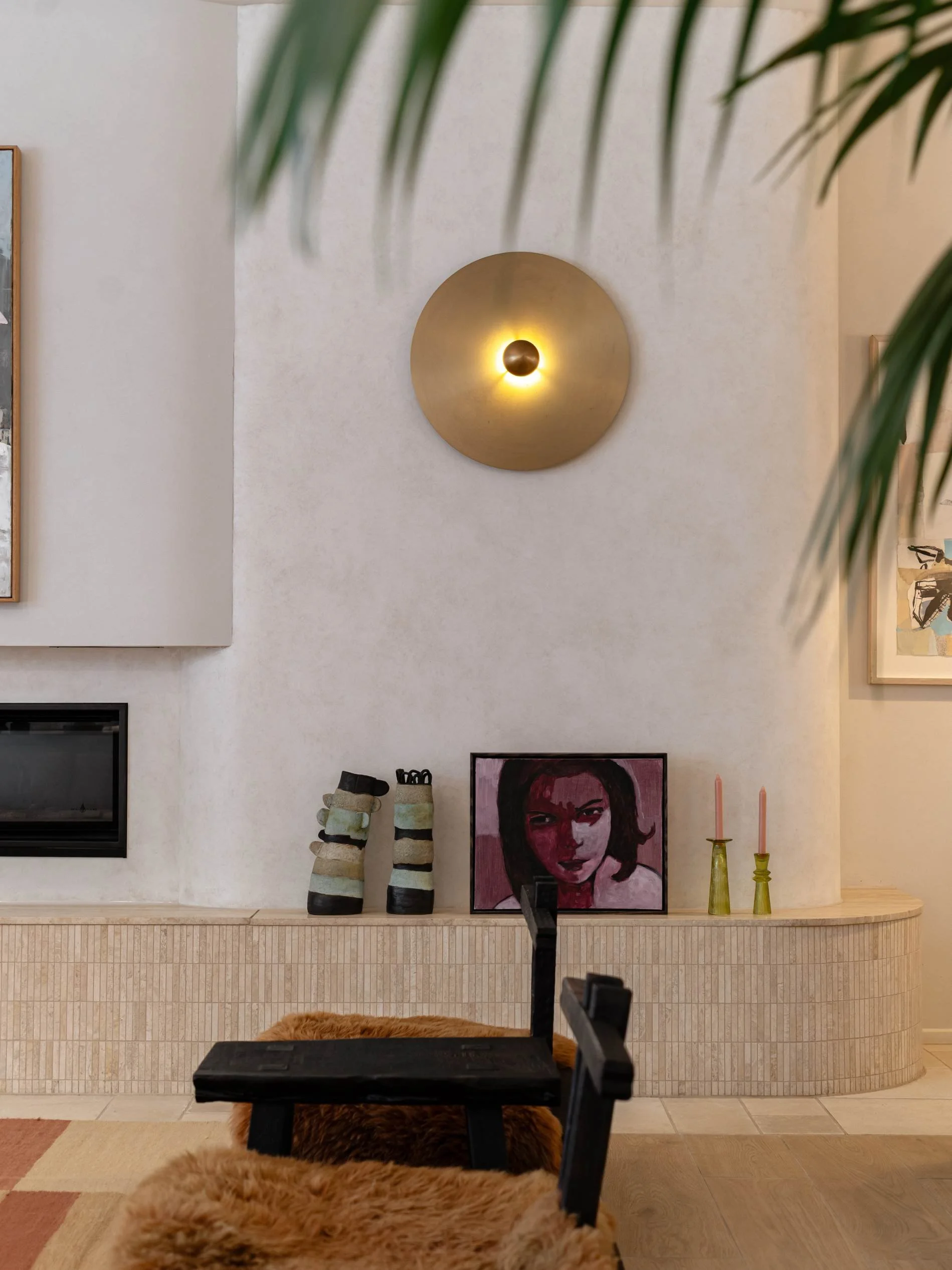 Living room with wall-mounted light fixture, framed artwork, boots, portrait painting, pink candles, and wooden furniture at Basq House Hotel in Byron Bay