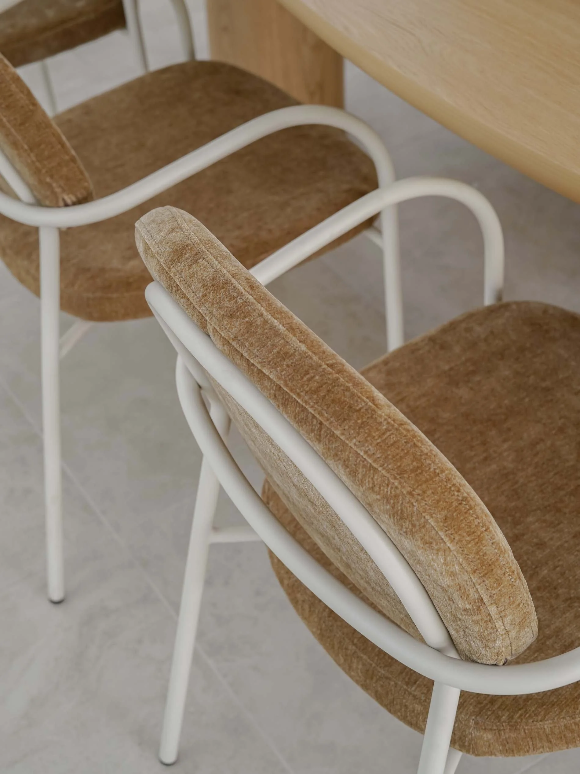 Close-up of two retro-style chairs with light brown textured fabric seats and backs, and white metal frames, placed around a light wood table in luxury property in Mermaid Waters, QLD