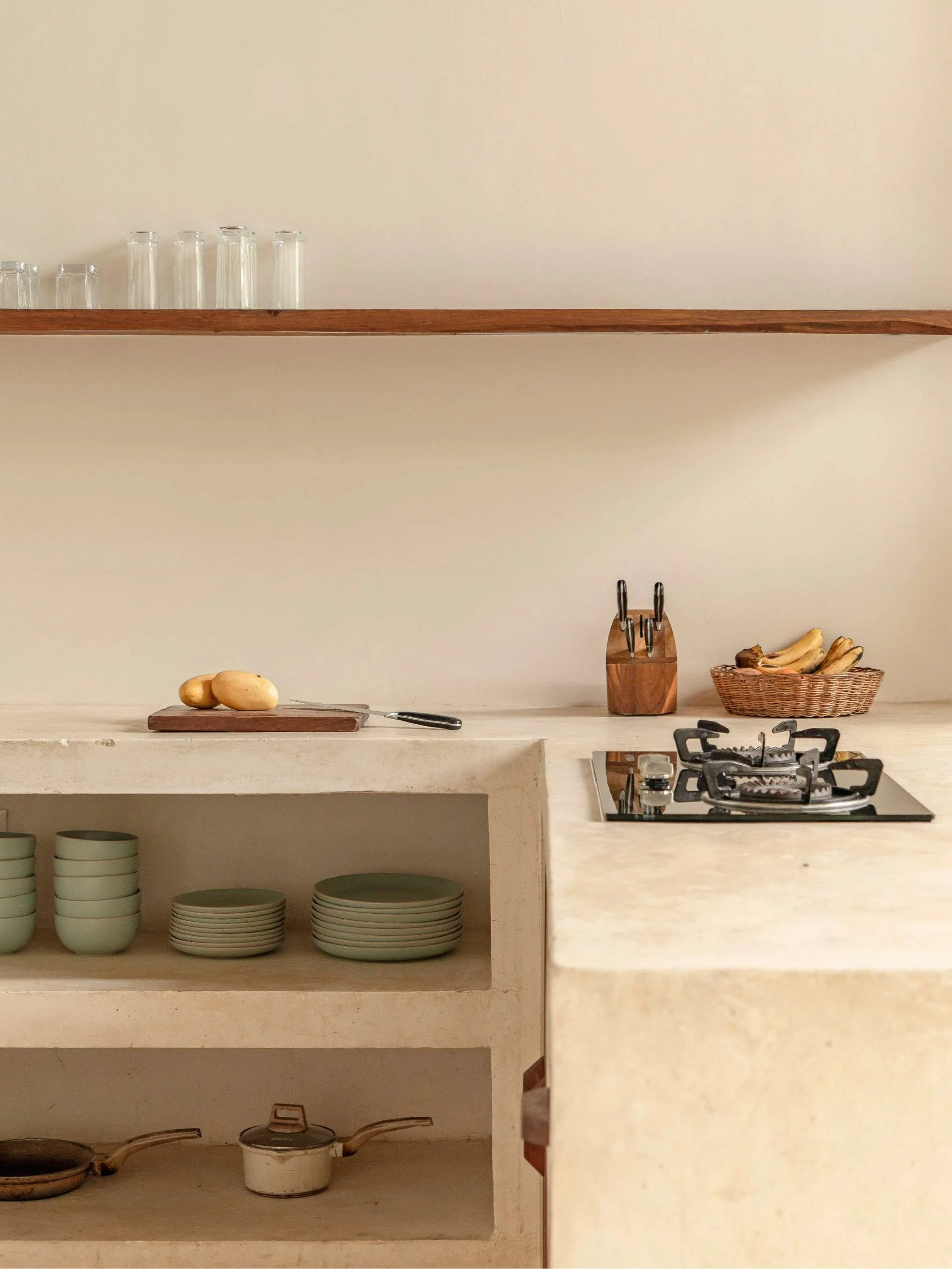 Minimalistic kitchen corner with a stovetop, a basket of bananas, a knife block, and a shelf with glassware and dishes, Villa Photography for beautiful accommodation in Siargao, Philippines