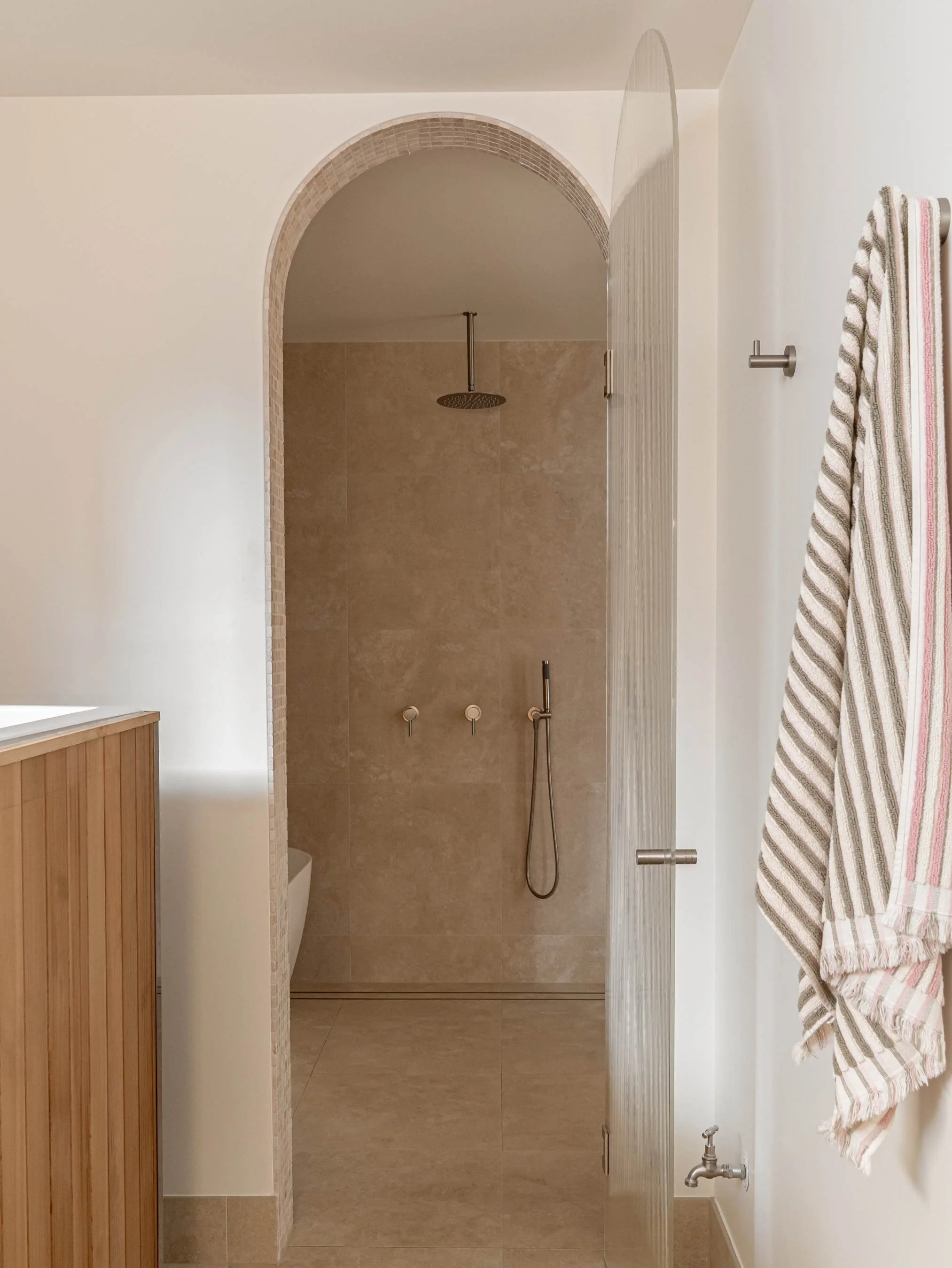 Modern bathroom with walk-in shower, beige tiles, and a striped towel hanging on a wall hook in the Ocean Ave Project in Tweed Heads, QLD