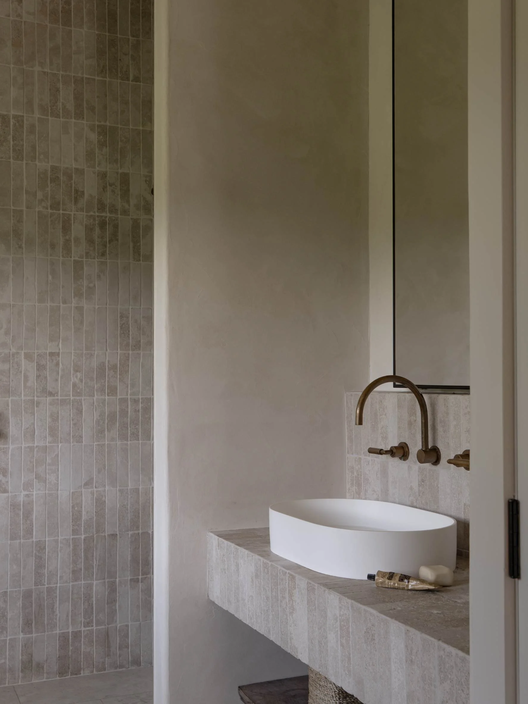 Modern bathroom with a white vessel sink and brushed bronze fixtures on a stone countertop, with a large mirror and tiled wall.