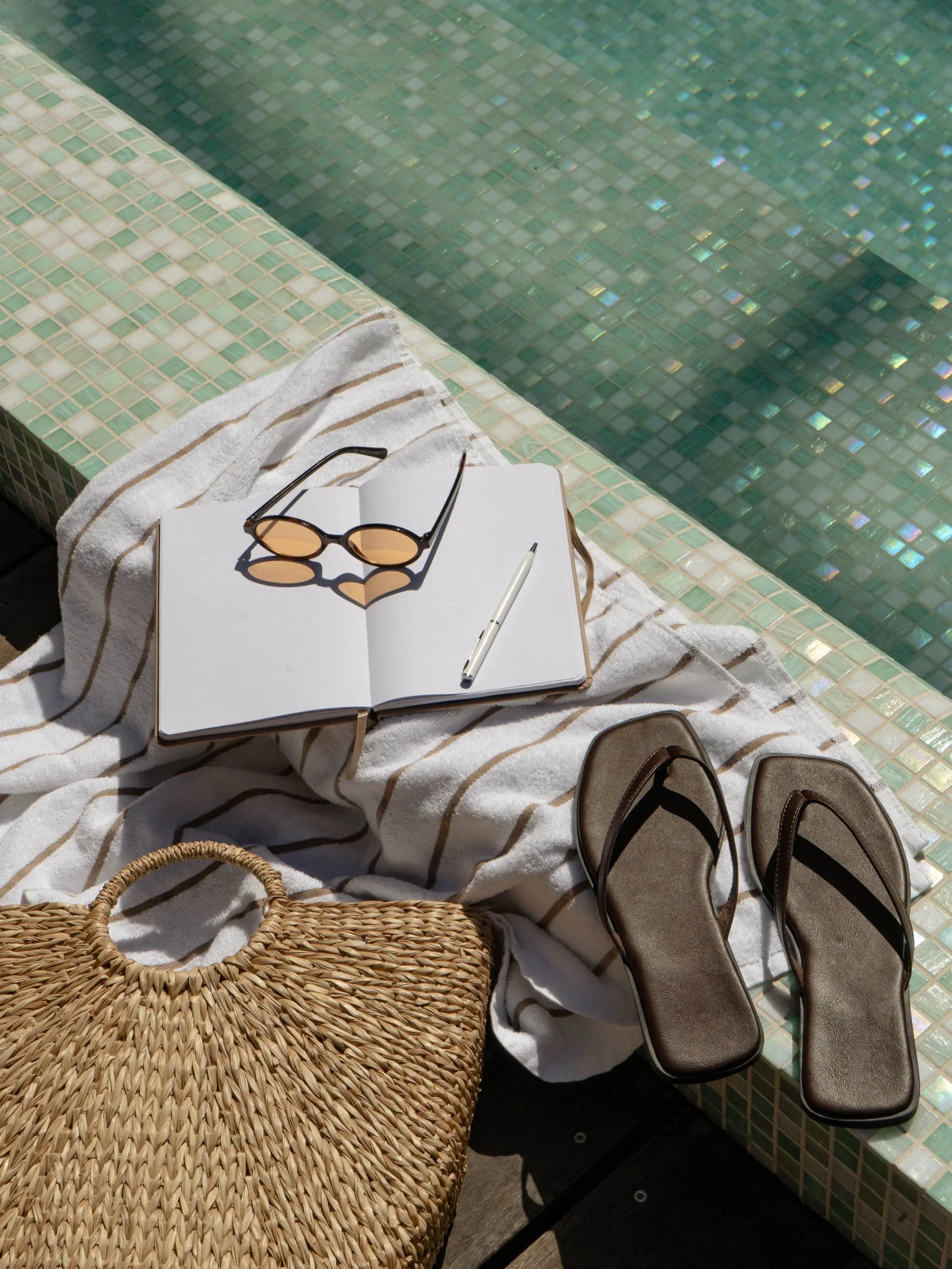 Poolside scene with open notebook, sunglasses, pen, and flip-flops on a towel next to a swimming pool at Basq House Hotel in Byron Bay
