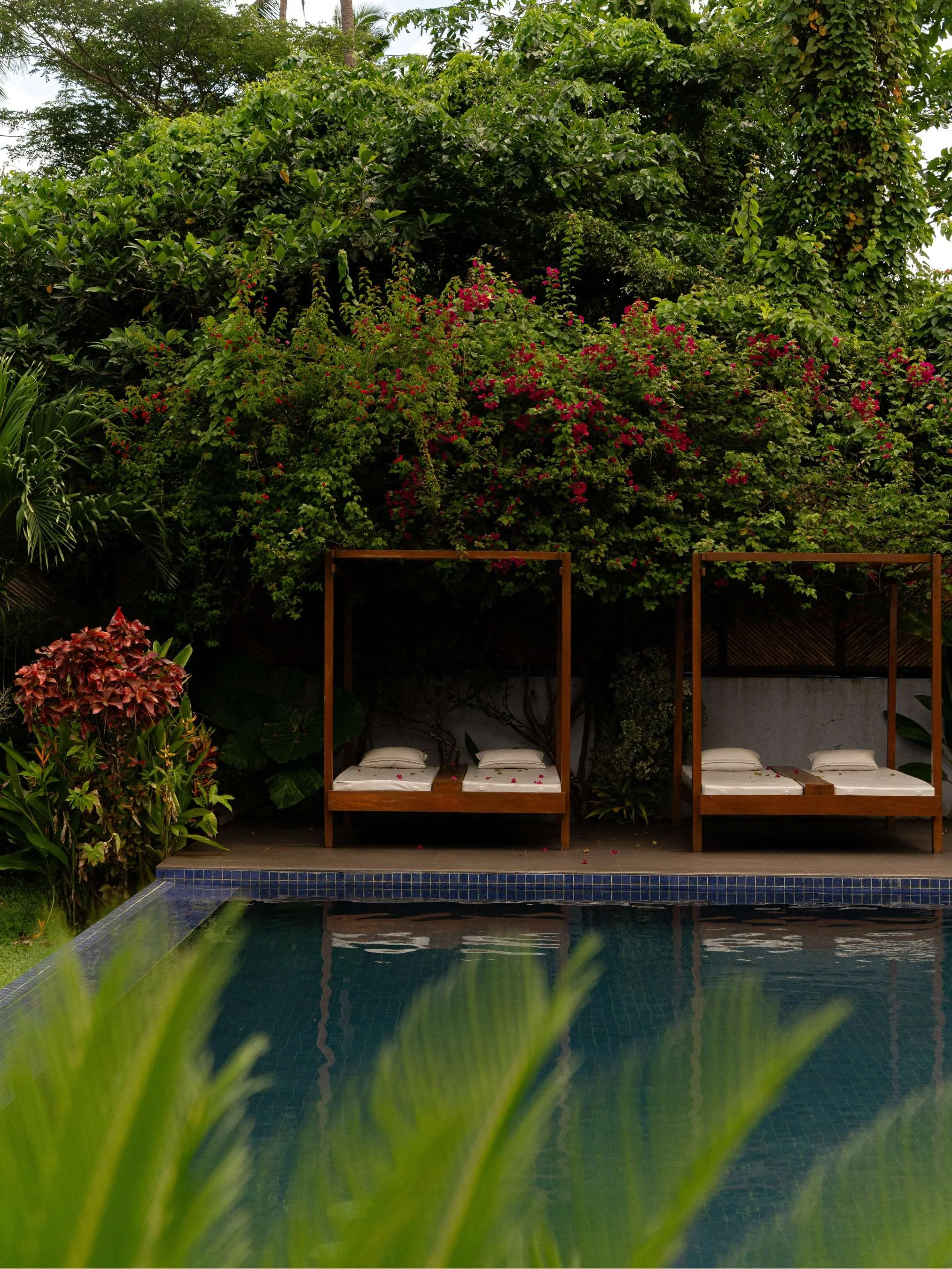 Poolside with two cabanas and white beds, surrounded by lush green tropical plants and trees at Anista Resort in El Nido, Philippines 