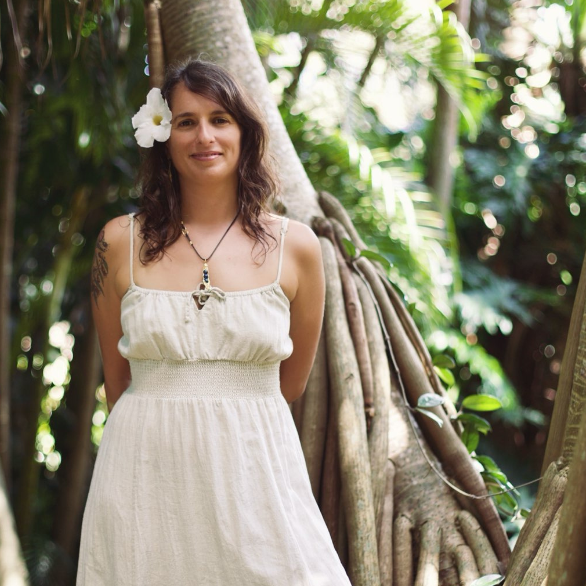Woman with a white flower in her hair standing outdoors in a lush green tropical jungle.