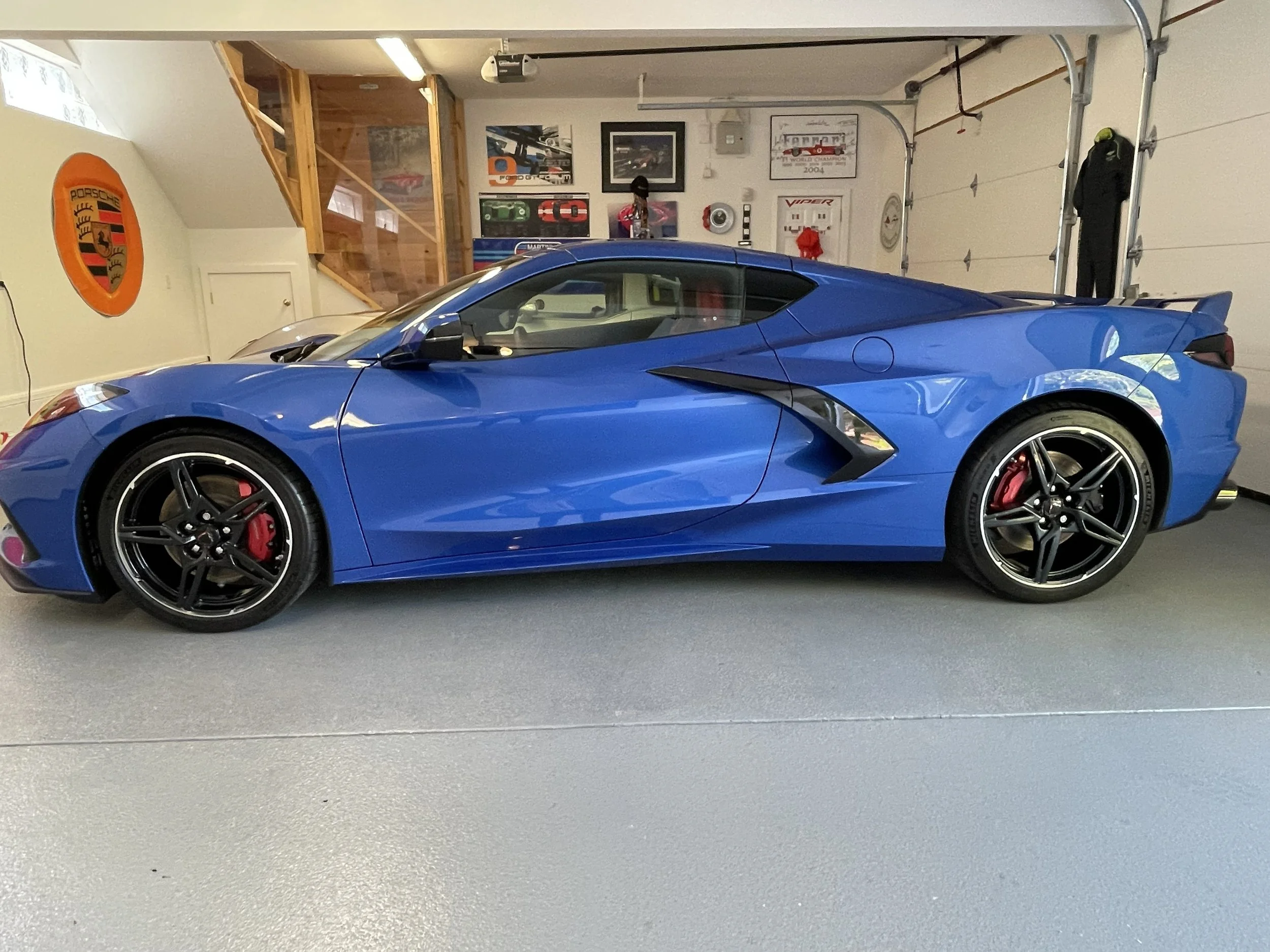 A blue sports car parked inside a garage with framed car memorabilia on the wall.