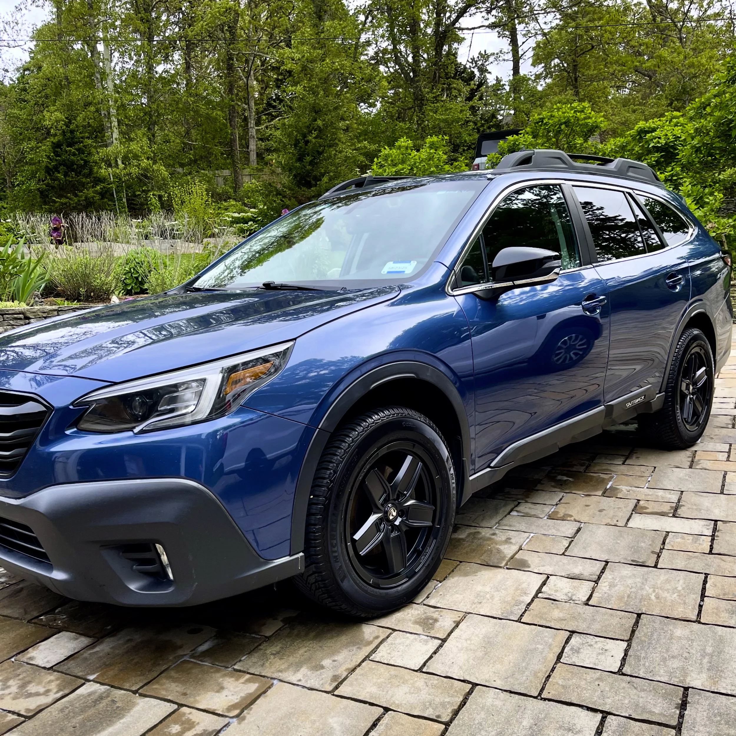 A blue SUV parked on a stone driveway surrounded by greenery and trees.