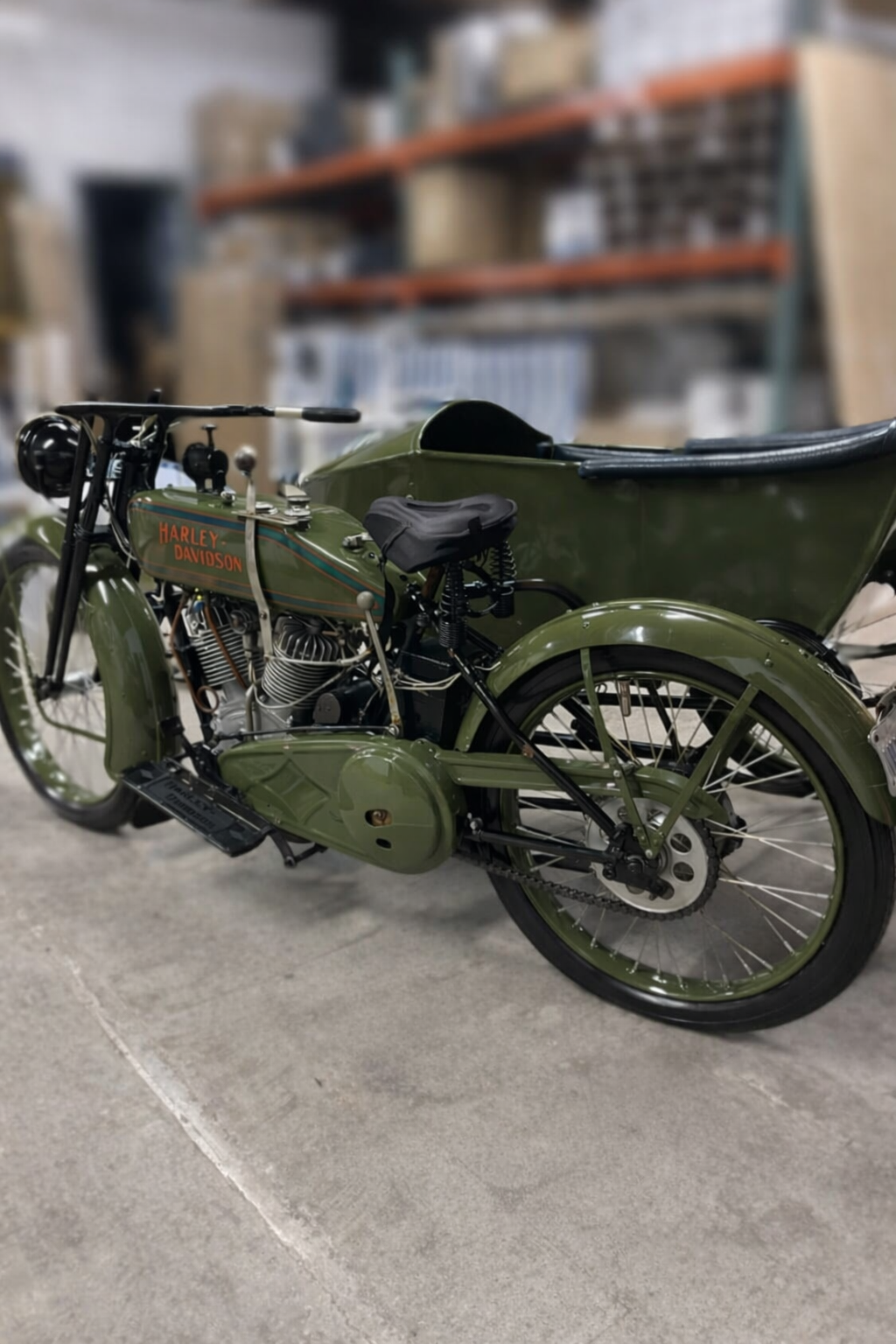 A vintage green Harley-Davidson motorcycle with a sidecar, parked on a concrete floor in a storage or workshop setting.