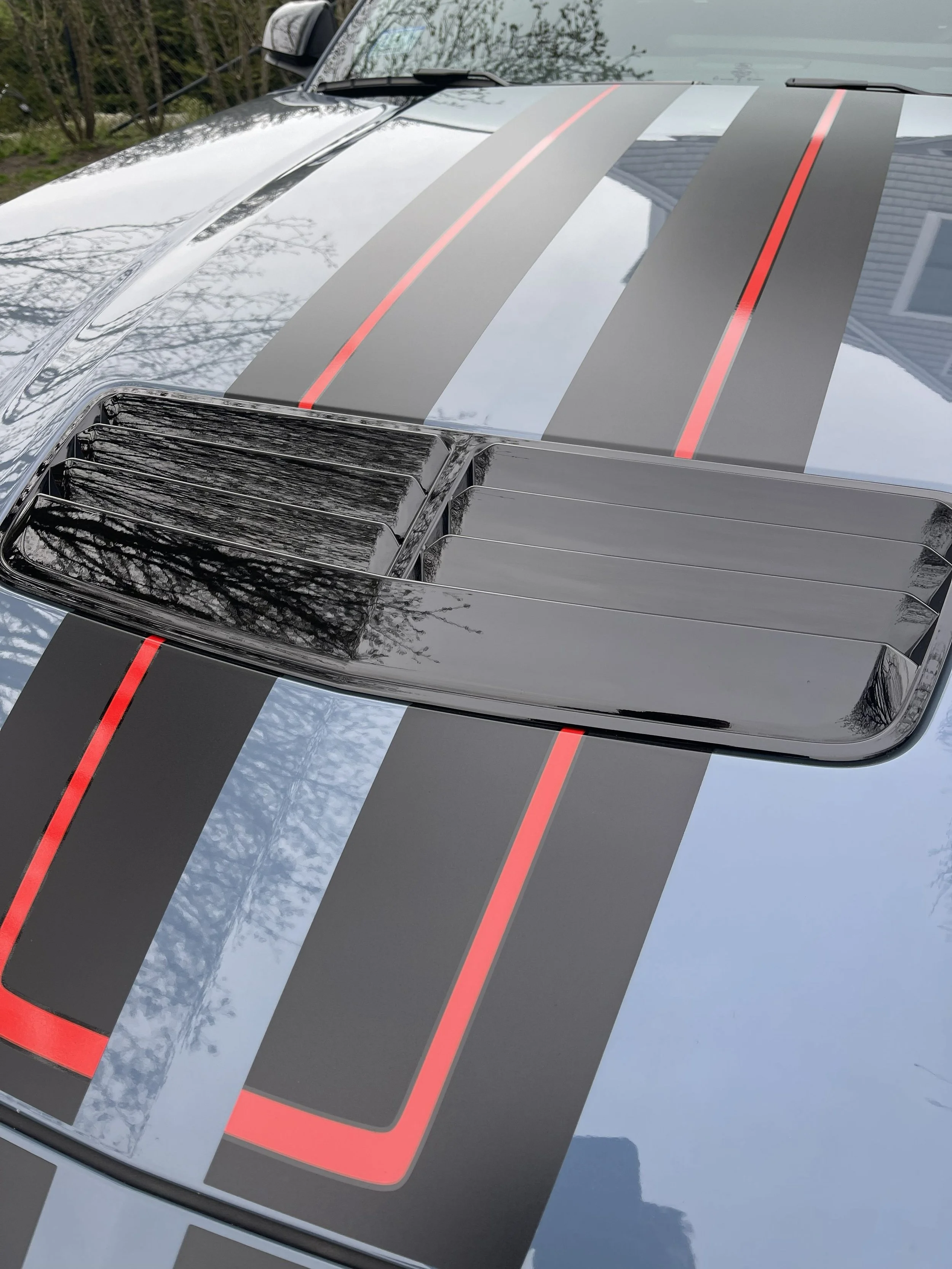 Close-up of a car hood with black and gray racing stripes accented with red lines.