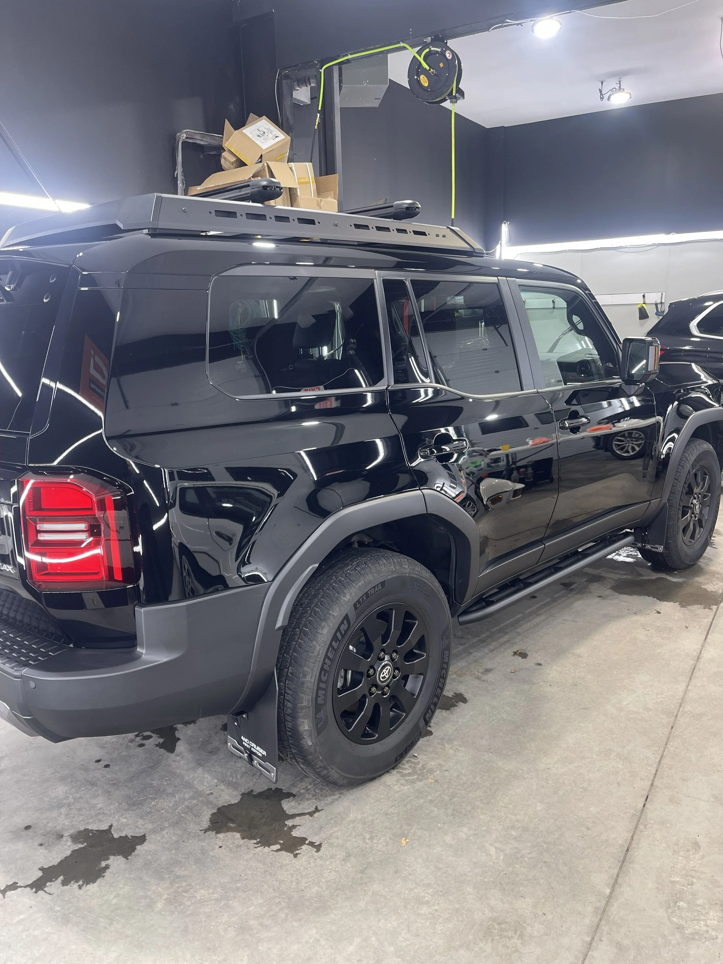 A black pickup truck parked inside a garage with a retractable hose reel and some cardboard boxes on a shelf above it.