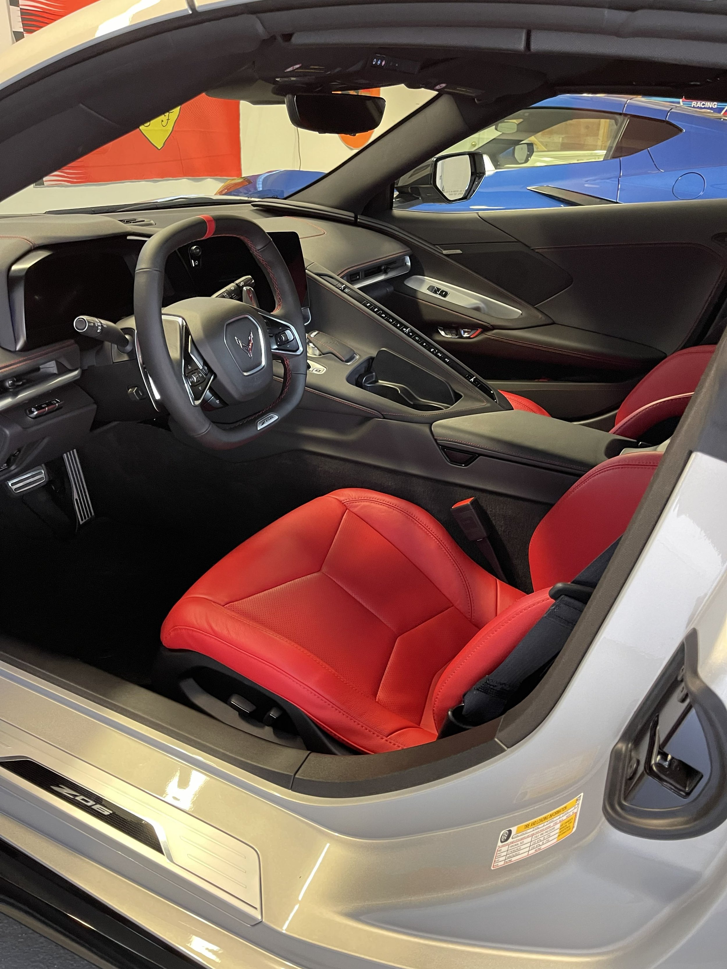 The interior of a sports car, featuring a black dashboard, steering wheel with the Chevrolet logo, red bucket seats, and a central control console.