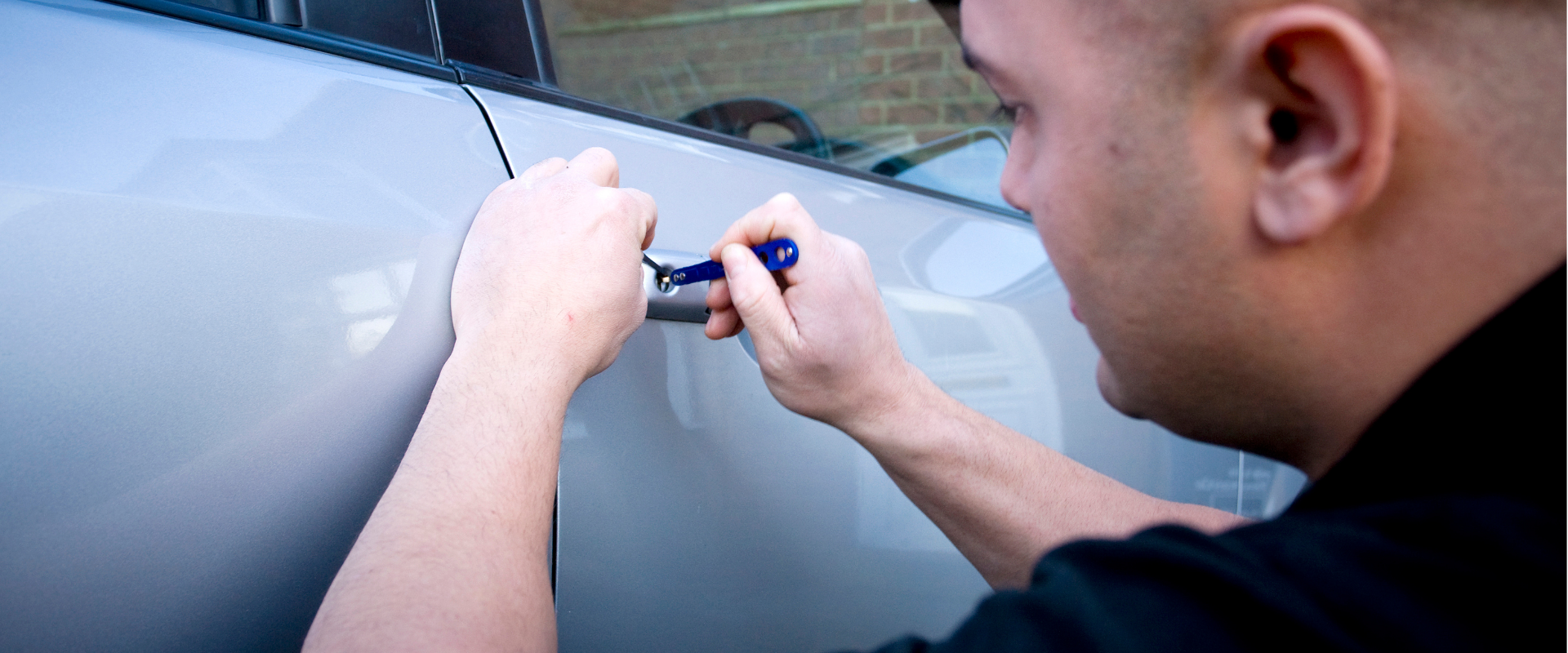 A person is using a small blue screwdriver to lock or unlock the door of a silver car.