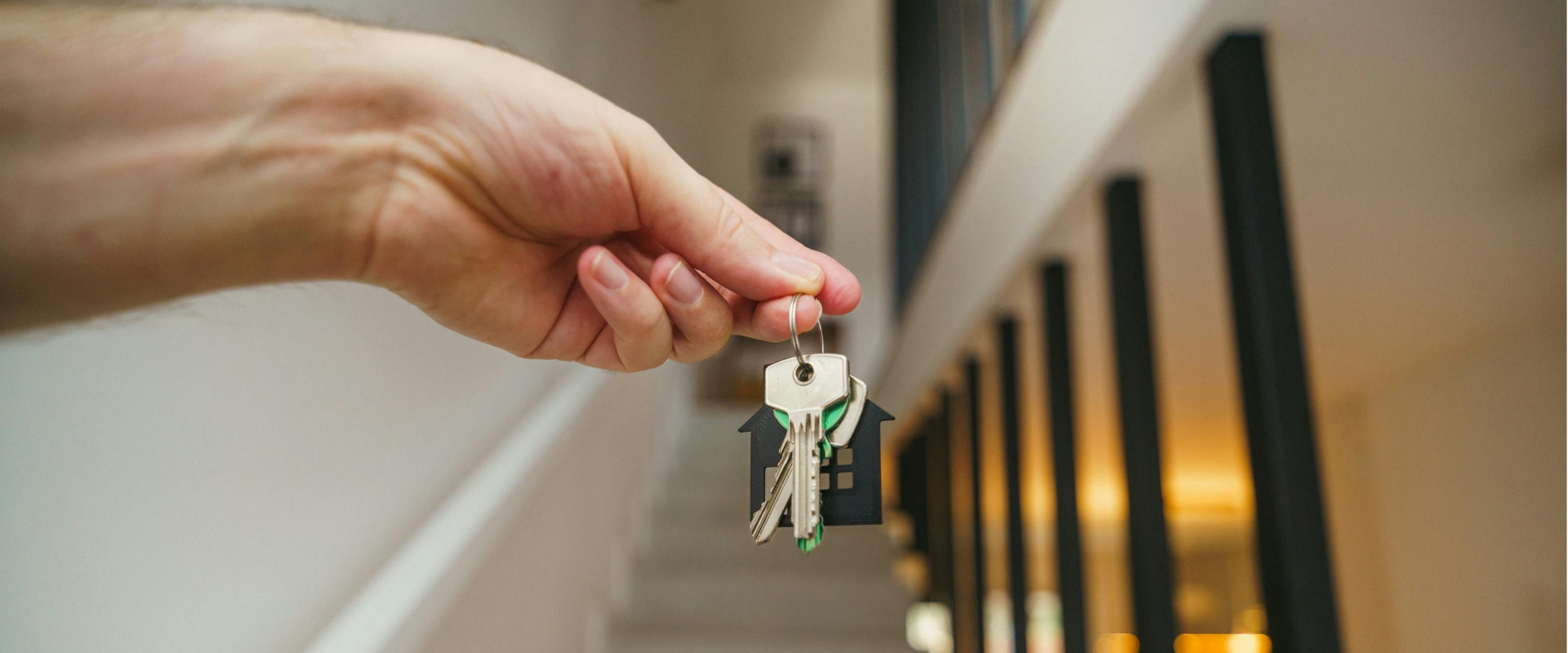 Hand holding a keychain with house-shaped key cover, hanging from a railing.