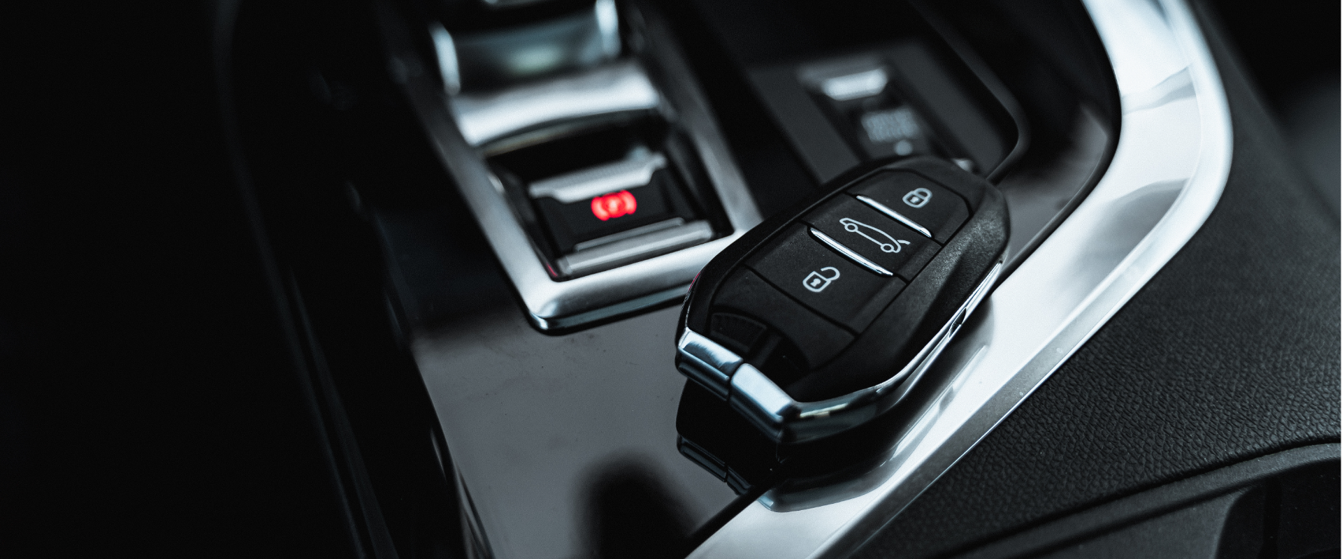 Close-up of a car key fob with lock, unlock, and trunk buttons on a car center console.