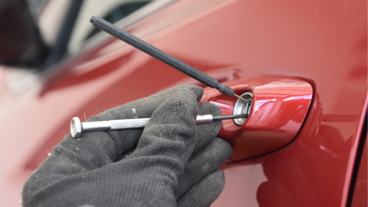A locksmith using professional picking tools to unlock a red car door handle.