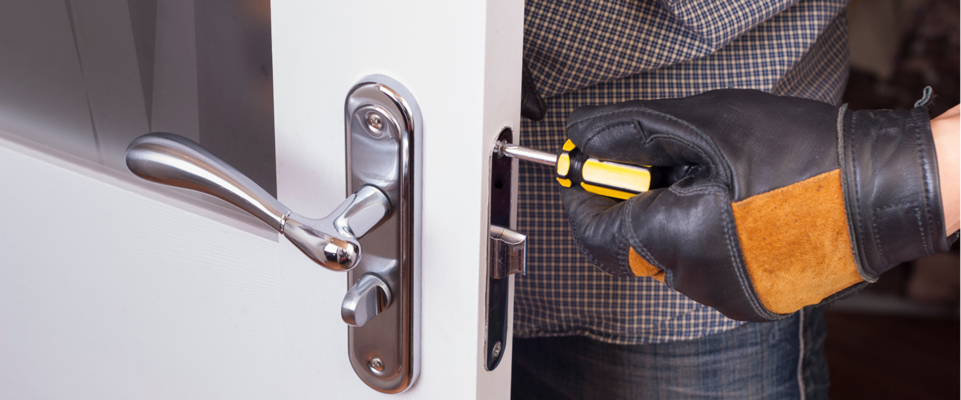 Person wearing black and orange work gloves using a screwdriver to install a door lock.