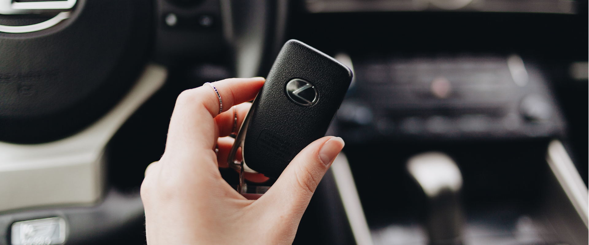 A person holding a black Lexus car key fob inside a vehicle, with dashboard and controls visible in the background.