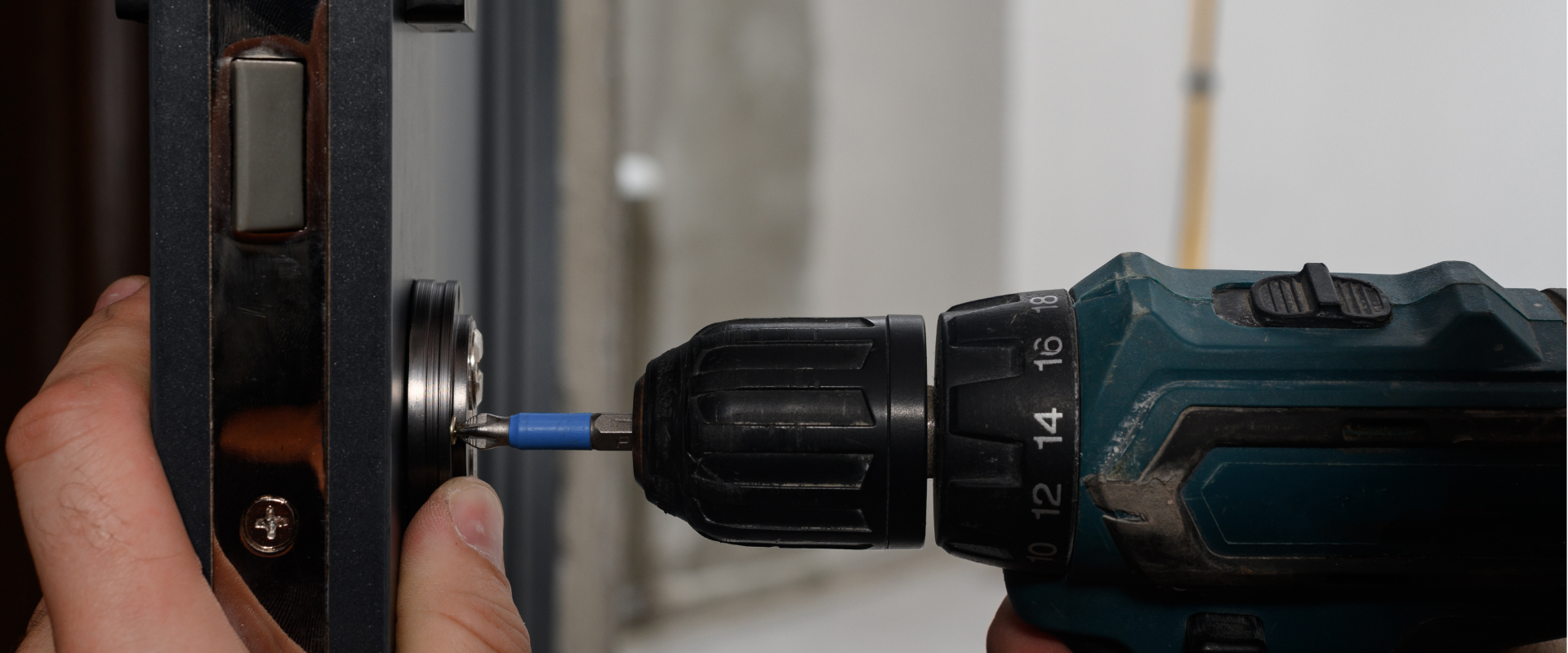 A person using a power drill to tighten or loosen a screw on a black metal panel.