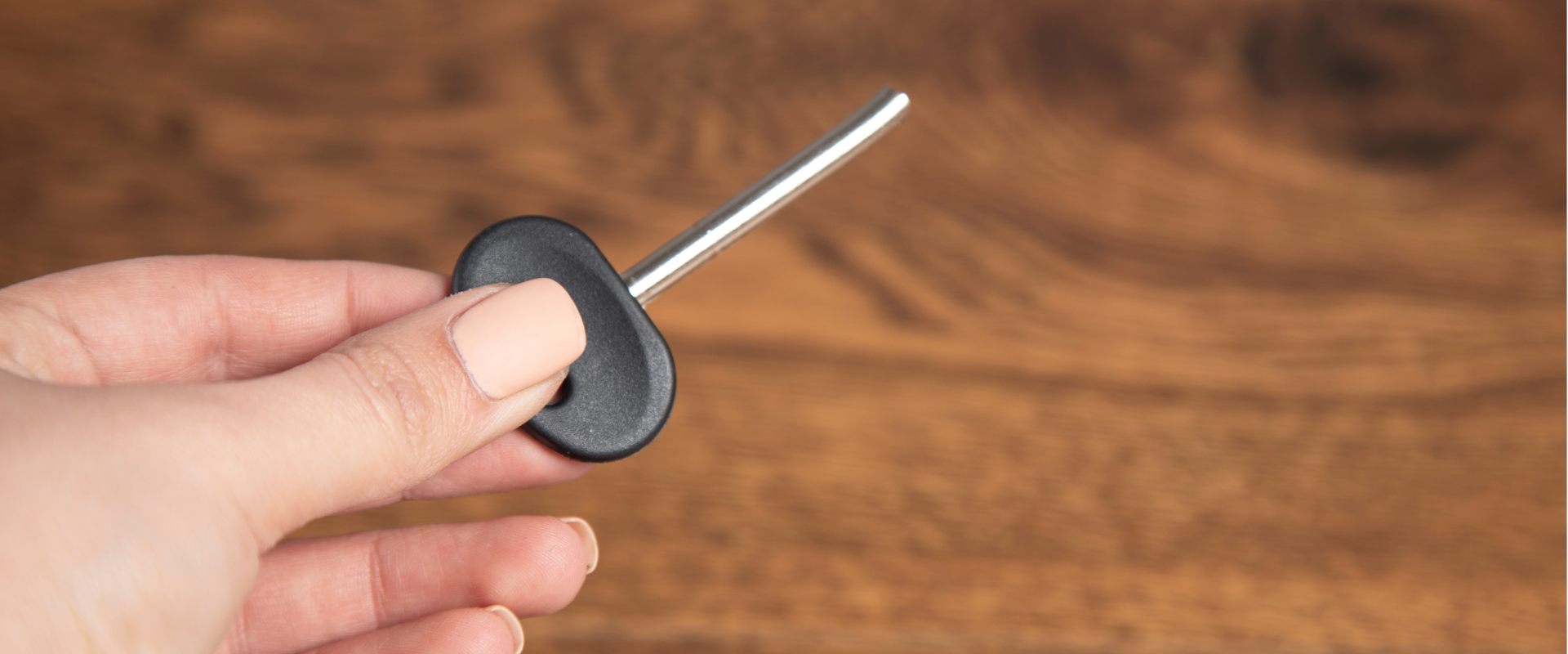 A person holding a small, silver, T-shaped metal tool with a black plastic handle against a wooden surface background.