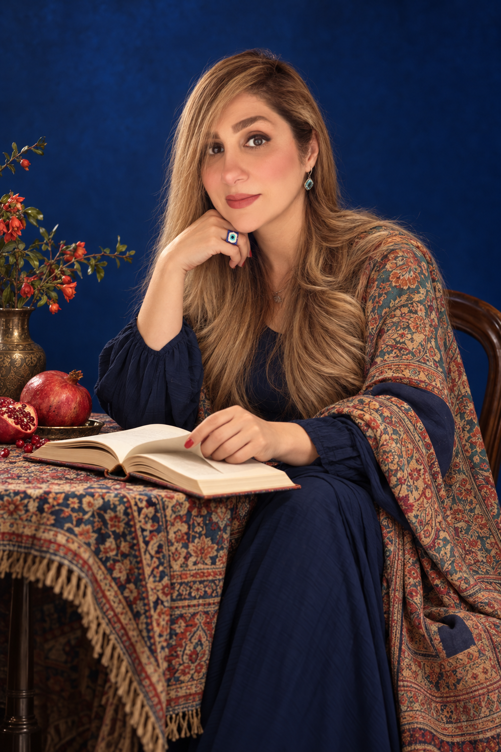 04 · Contemporary Yalda
A flowing navy dress and richly patterned shawl against deep blue light. Seated beside pomegranates and an open poetry book, a quiet, thoughtful pose creates a personal story of memory, warmth, and cultural connection. AI-gene