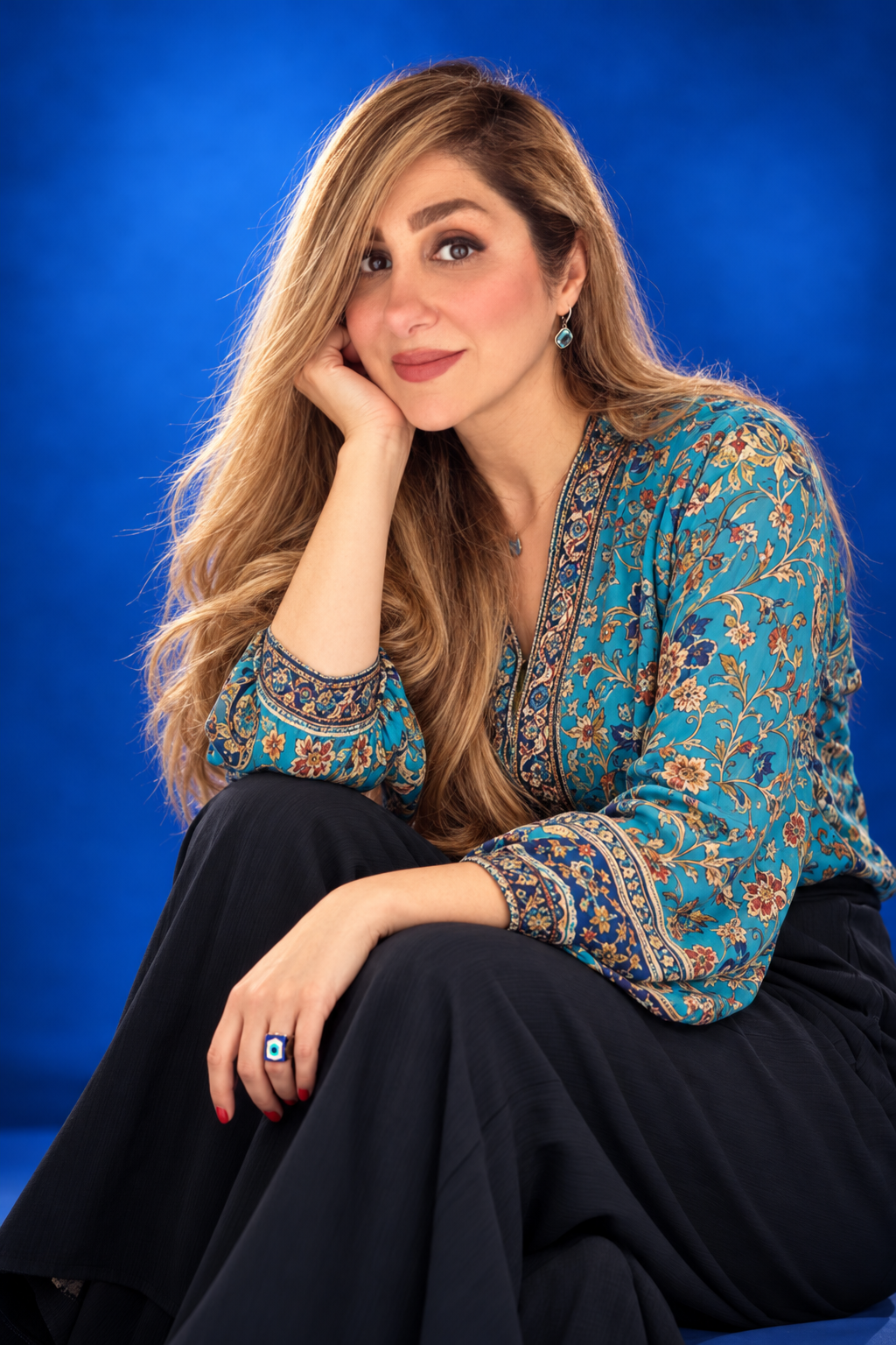 10 · Artist at Ease
A turquoise patterned blouse and black trousers against a blue LED background. A relaxed seated pose, knee lifted and hand lightly supporting the face, brings warmth and personality to the artist’s presence. AI-generated shoot con