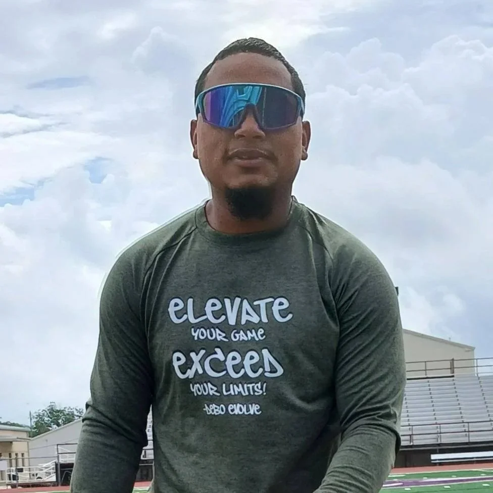 A man wearing sunglasses and a gray long-sleeve shirt with motivational text, standing outdoors on a cloudy day.