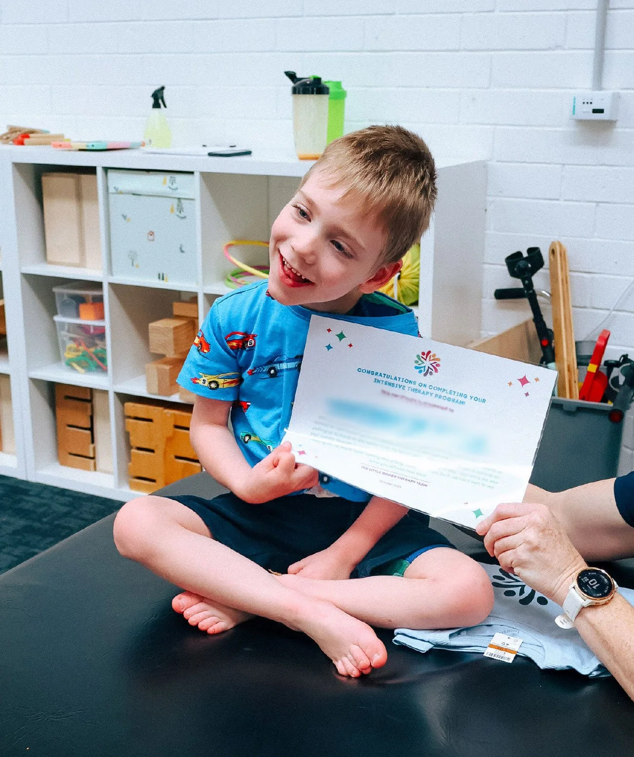 Child smiles holding their certificate for completing a block of intensive therapy