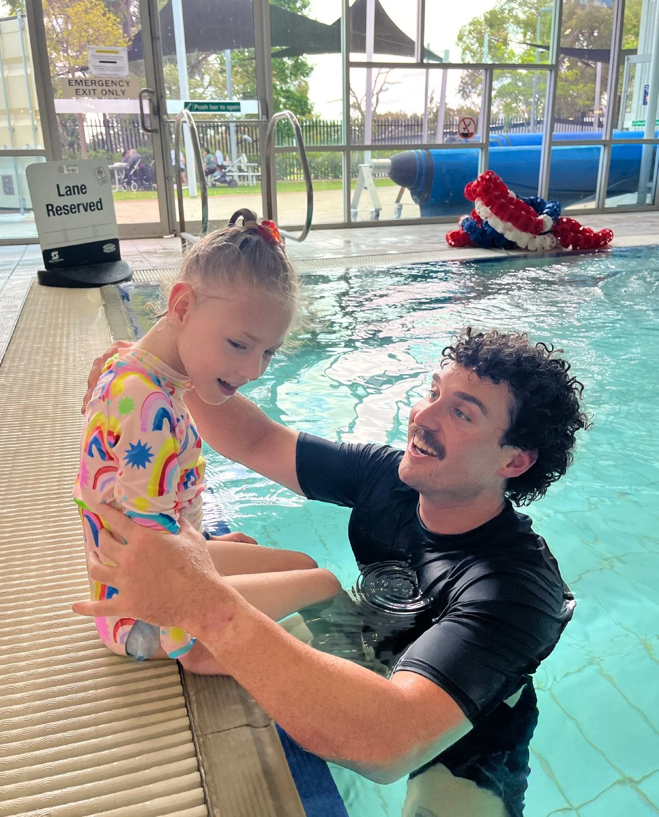 Child supported by a therapist during a hydrotherapy session in a warm water pool at Little Bodies Therapy
