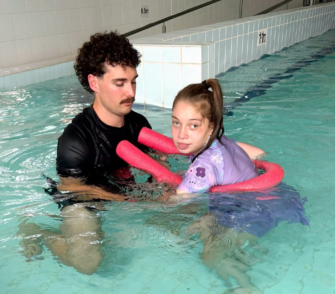 Child engaging in gentle water movement exercises with support from a hydrotherapist