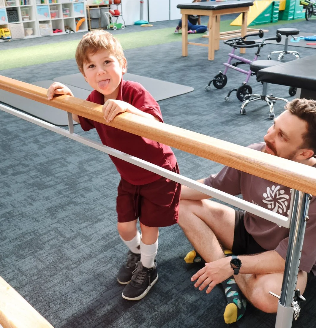 Child practising balance and standing at parallel bars with therapist support