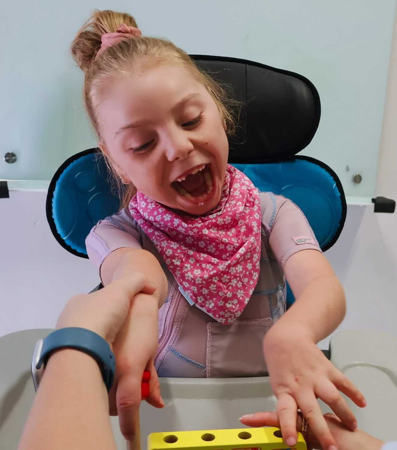 Child reaching forward during a hands-on therapy activity with therapist support