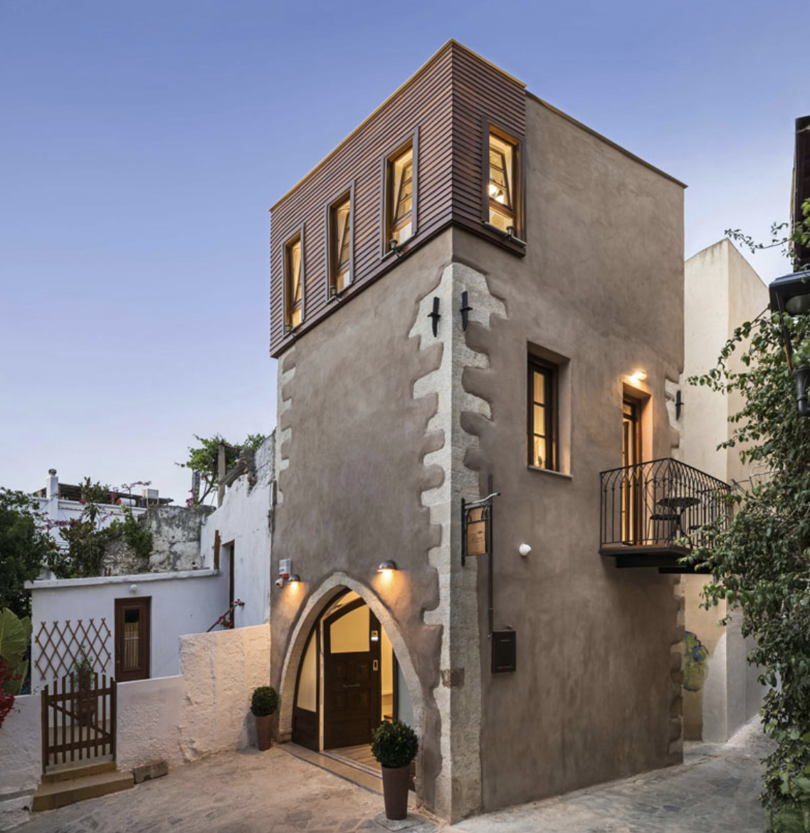 A multi-story Mediterranean-style house with a stucco exterior, arched entrance, and wooden accents at dusk.