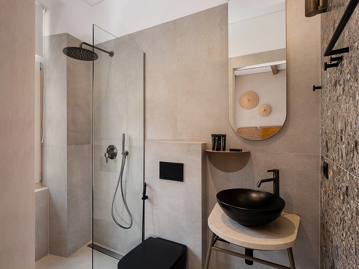 Modern bathroom with a walk-in shower, black vessel sink on a light countertop, mirror above the sink, and decorative wall art with woven circular pieces.