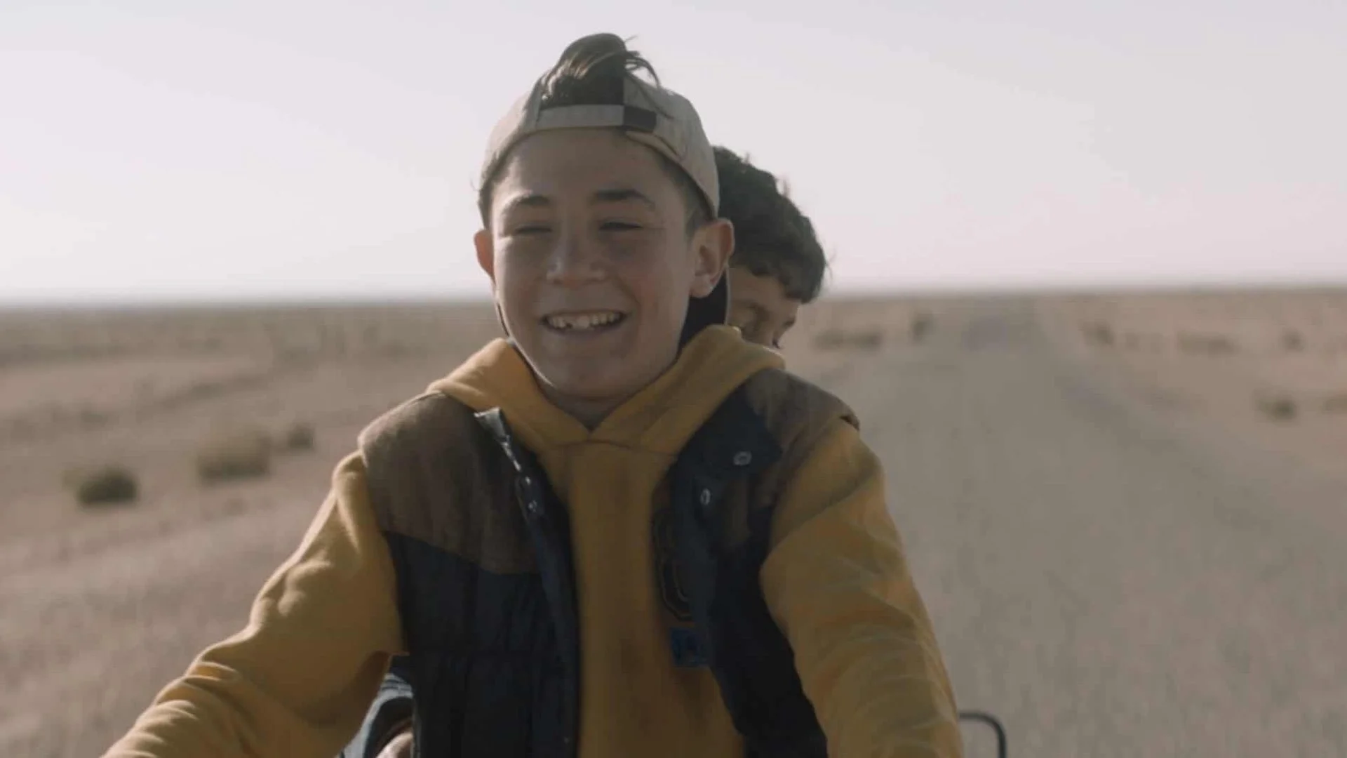 Two young men riding bicycles in a desert landscape, smiling and enjoying their time.