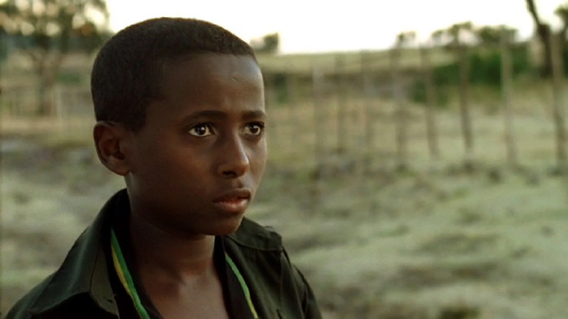 A young boy with short hair and a dark jacket looking thoughtfully into the distance outdoors.