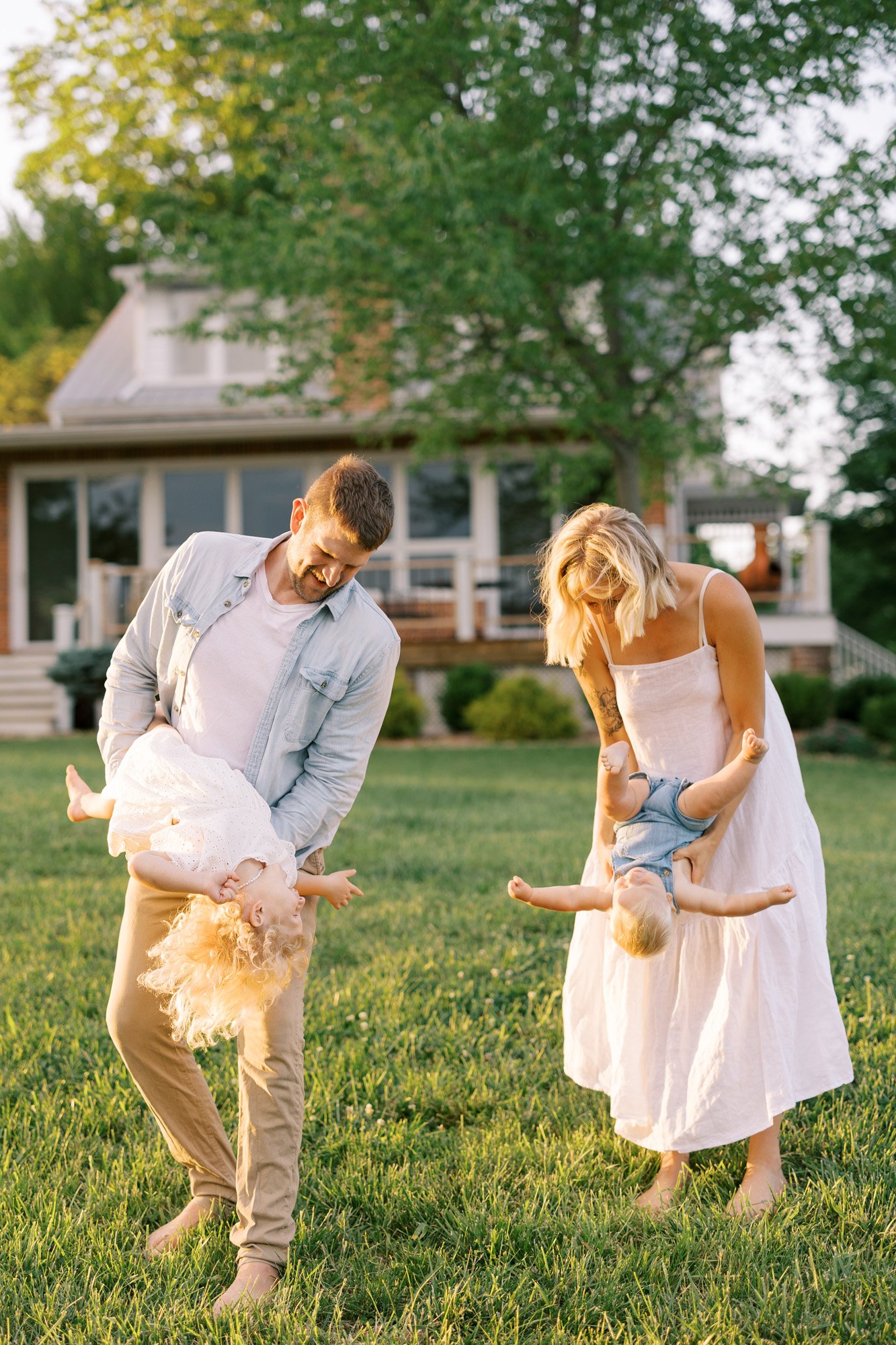 Parents playing with and holding two kids in front of a house outside