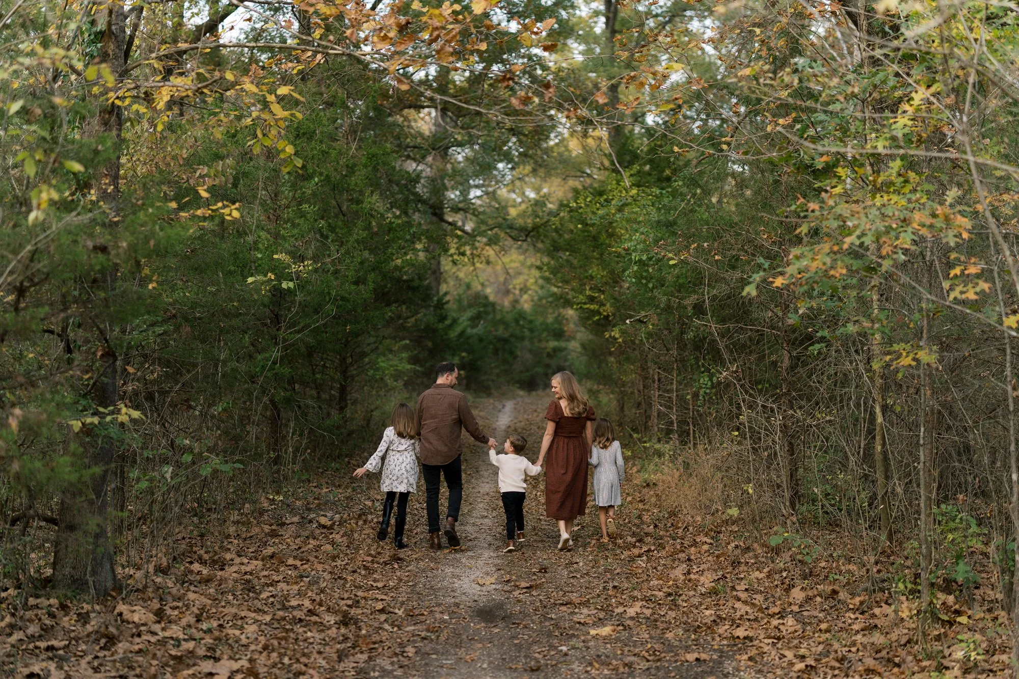 Family of 5 walking down tree-covered trail in a park during photo session