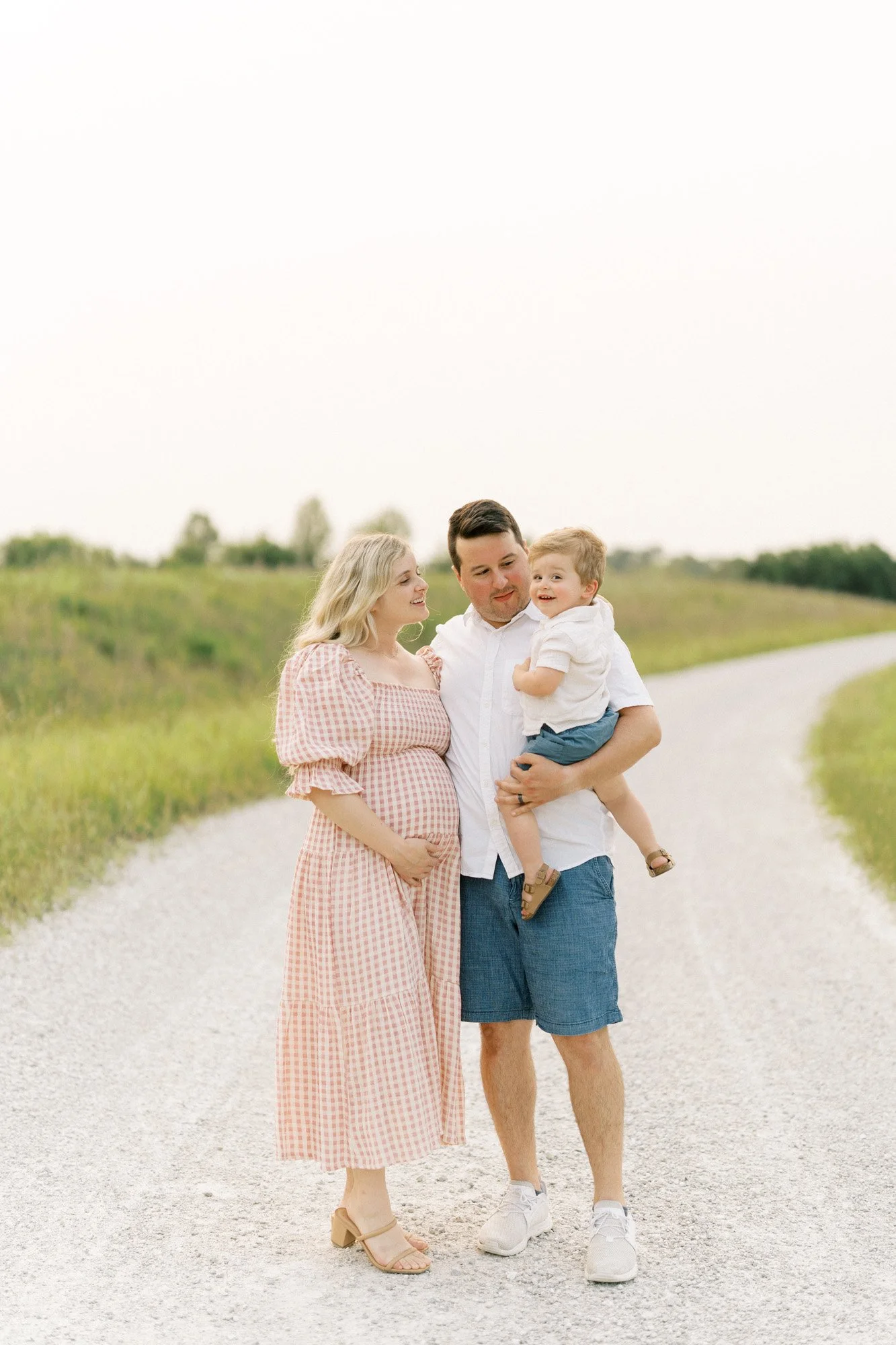 Expecting mom and Dad holding toddler boy on gravel path outside
