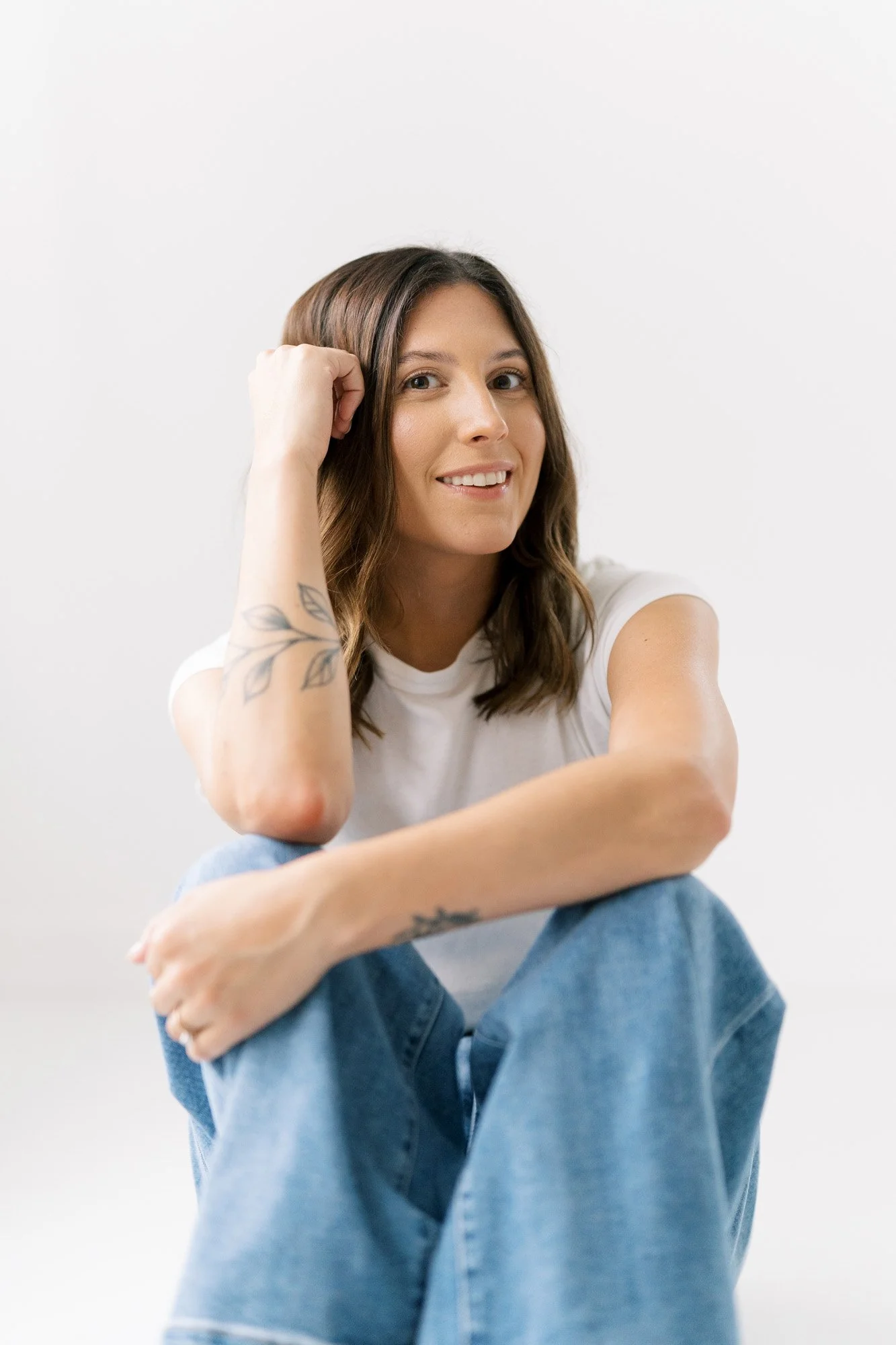 Tristan sitting on the floor of her studio with one arm across her bent knees and one hand on her head, smiling