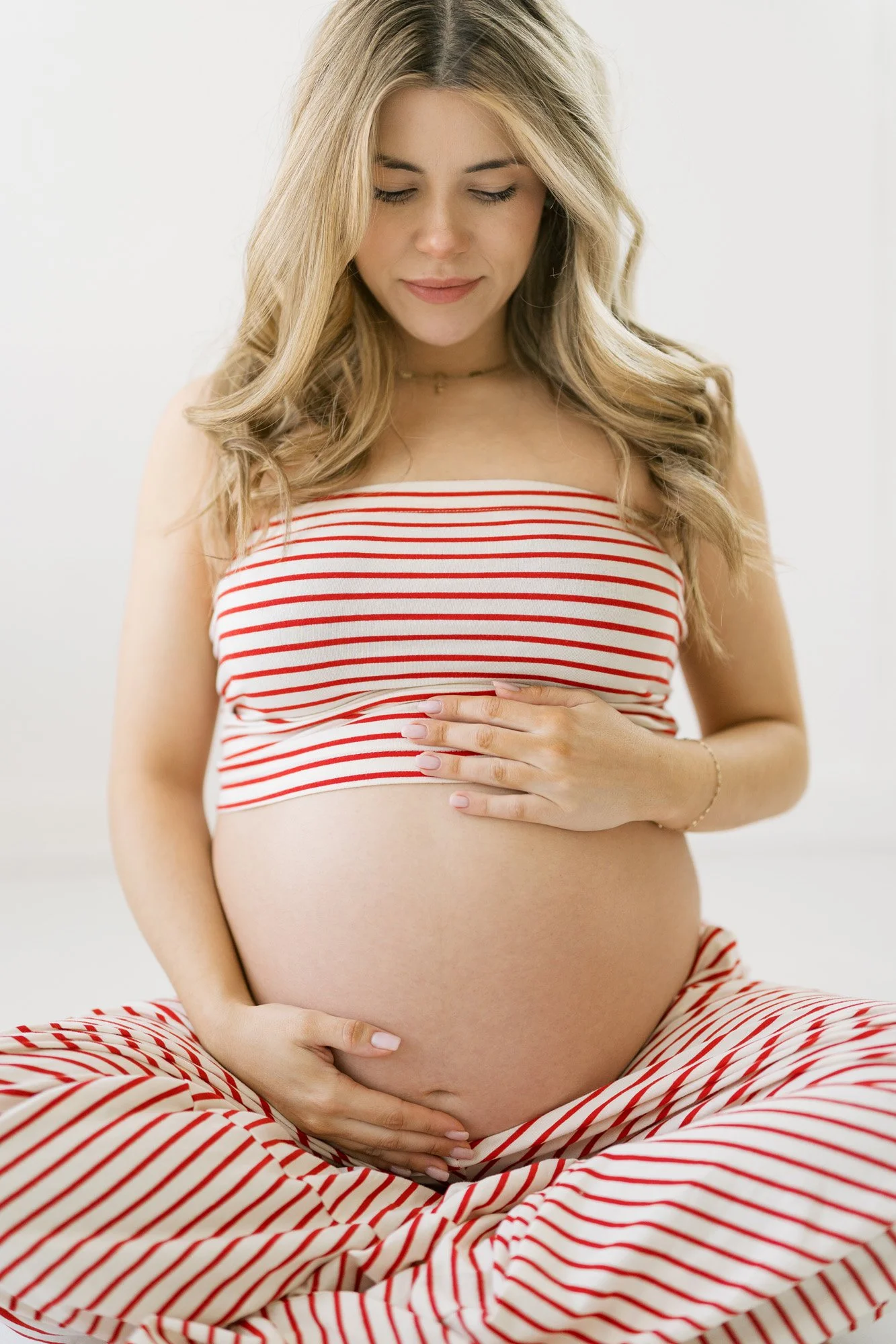 Pregnant woman in studio for maternity shoot, wearing red striped lounge pants and top