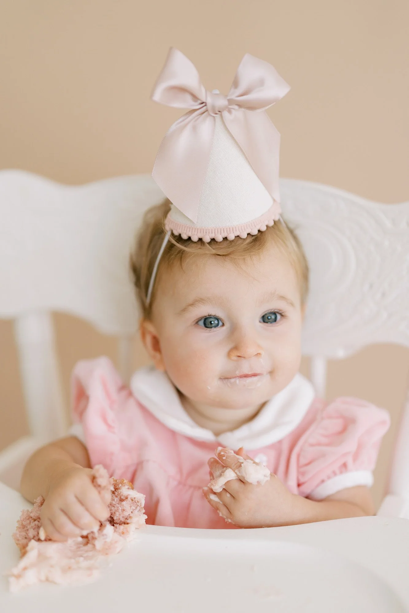 One year birthday session for a girl with a pink party hat and smash cake in a white high chair in a studio
